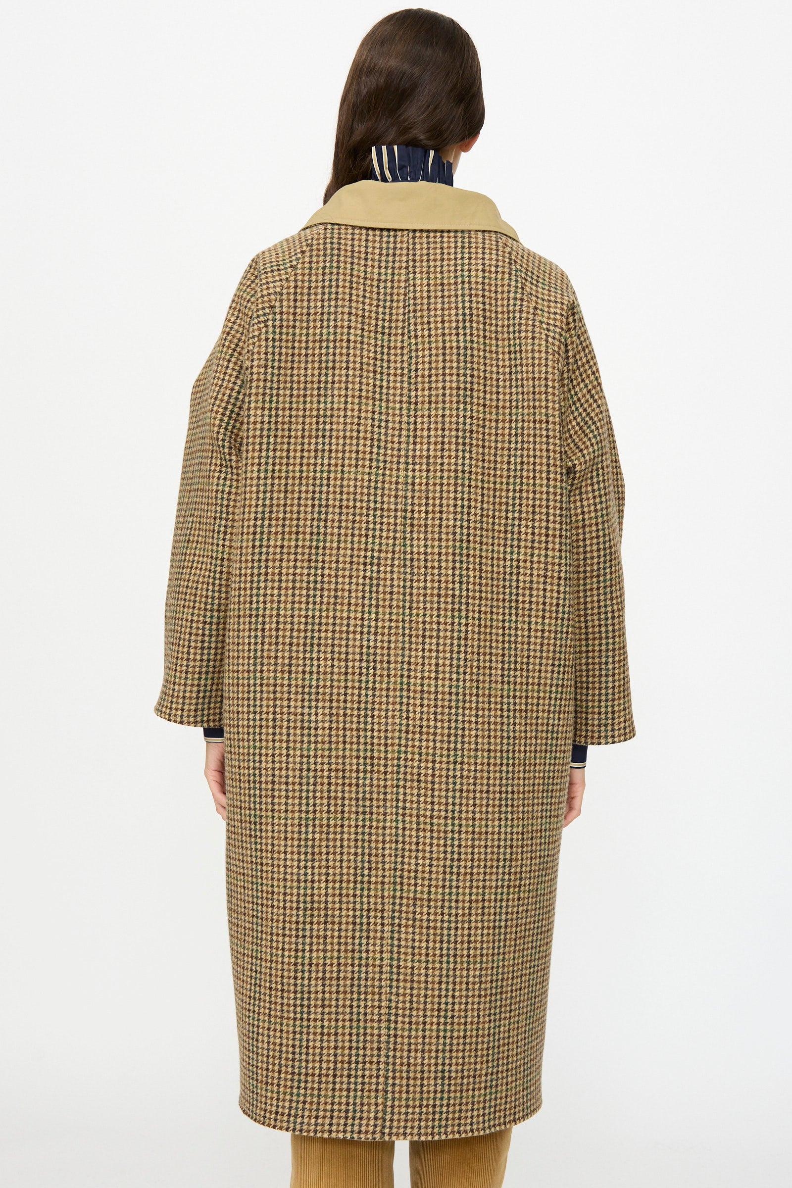 A person faces away, wearing the Les Prairies De Paris Dickens Moon Reversible British Trench in taupe. The long overcoat features a collar and a plain white background.