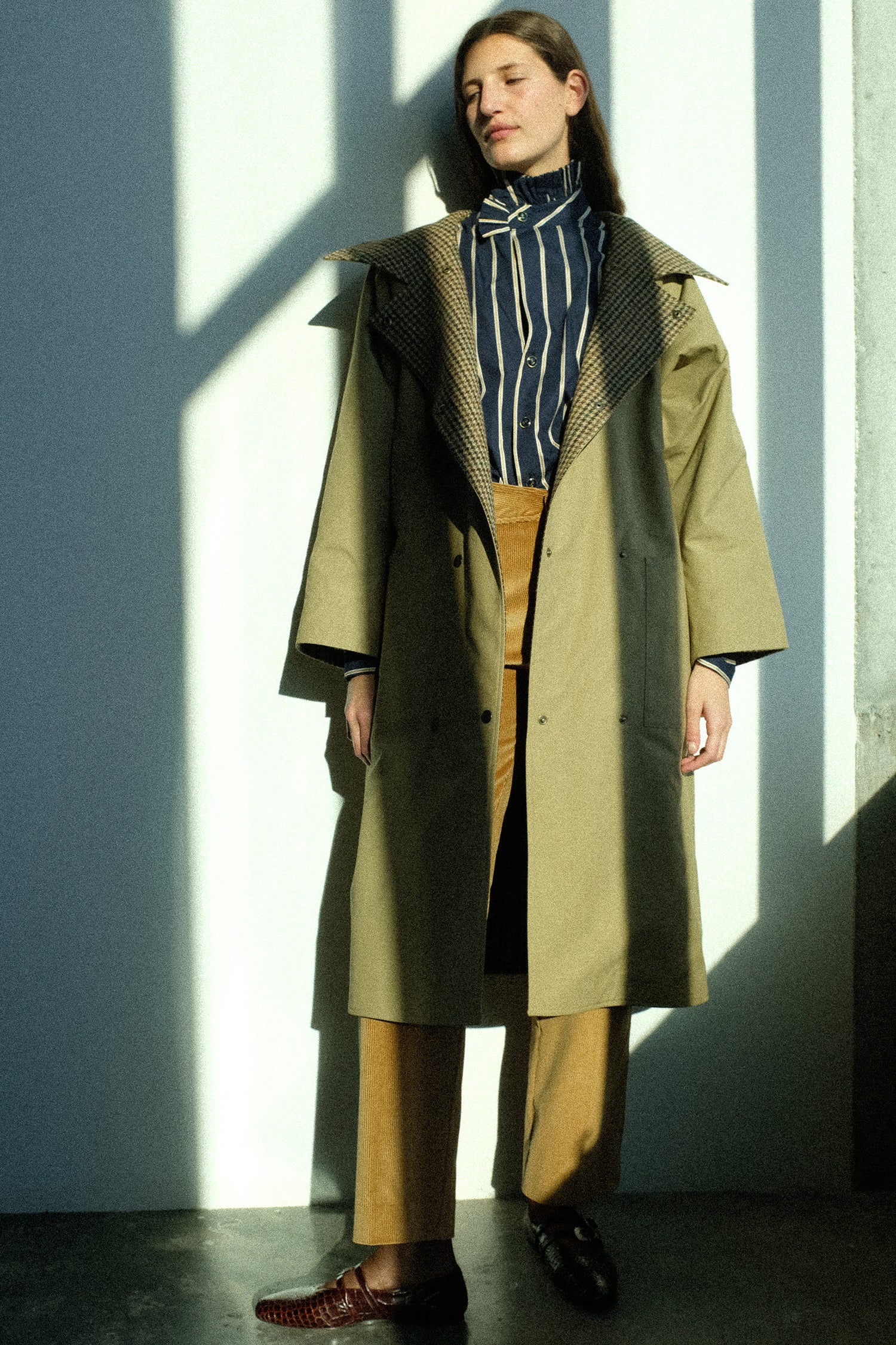 A woman wearing pieces from Les Prairies De Paris FW25 collection against a sun-filled wall.
