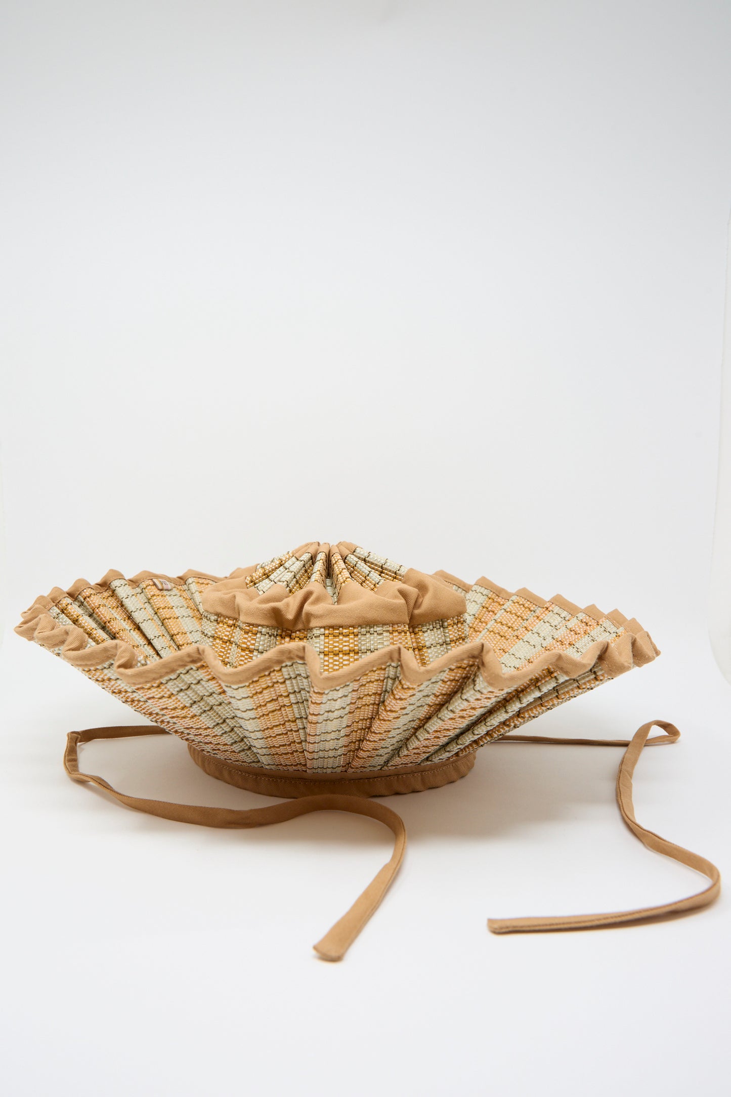 The Island Capri Maxi Hat in Petra by Lorna Murray is a pleated sun hat made of natural grass fibers with a wide, structured brim in beige and light patterns, two long ties, UPF 50+ protection, shown on a white background.