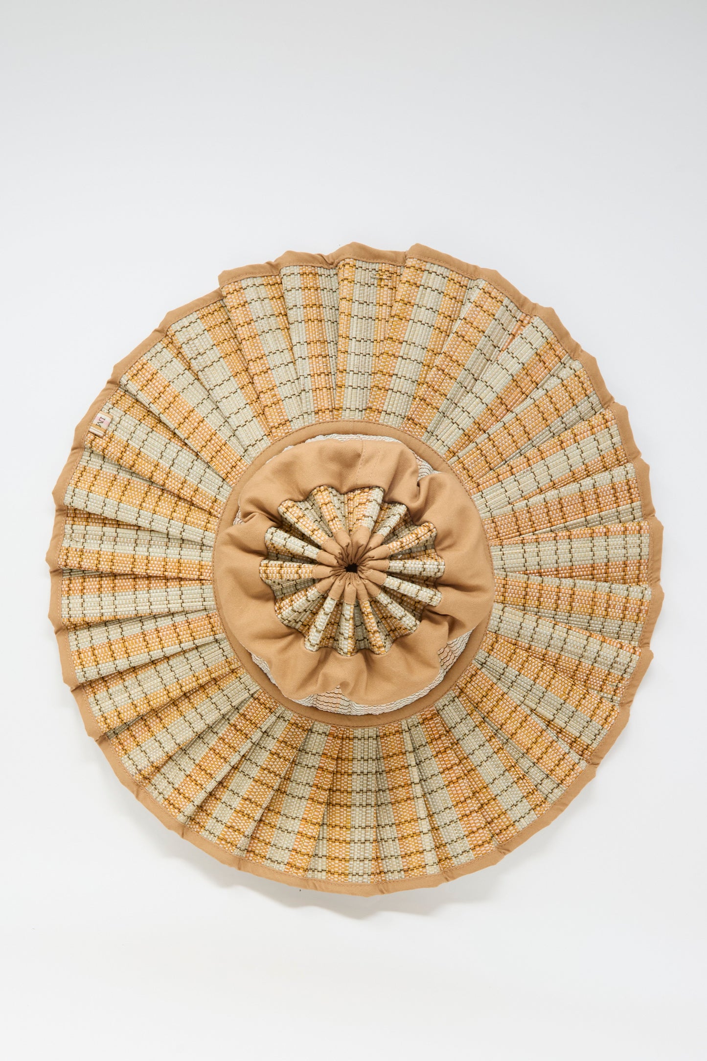 The Island Capri Maxi Hat in Petra by Lorna Murray is a round, woven sun hat in beige and tan, crafted from natural grass fibers with a pleated brim and gathered fabric center, offering UPF 50+ protection. Shown on a plain white background.