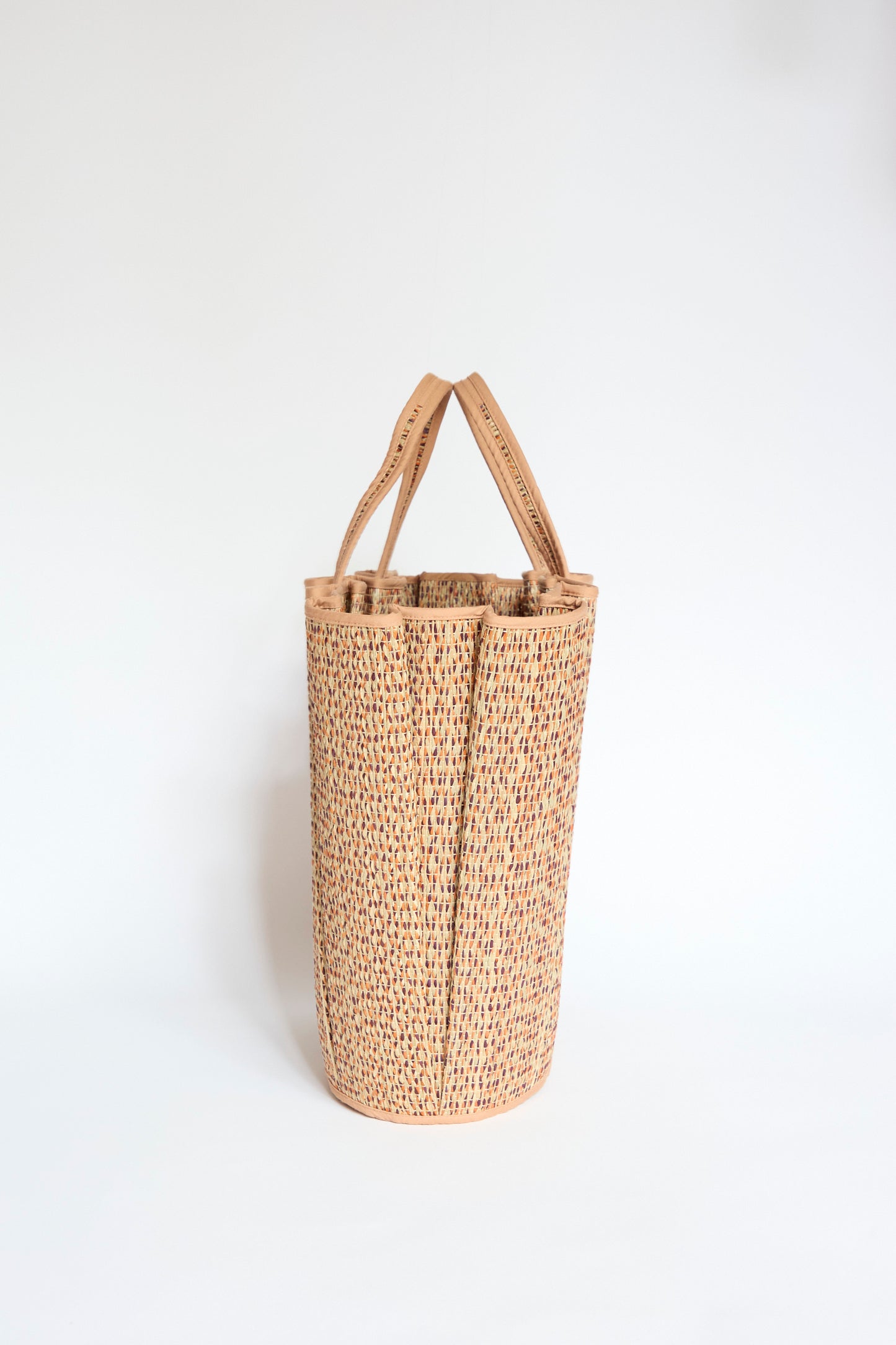The Lorna Murray Tropez Tote in Dawn, crafted from natural grass fibre with a textured pleated weave, stands upright with two handles against a plain white background.