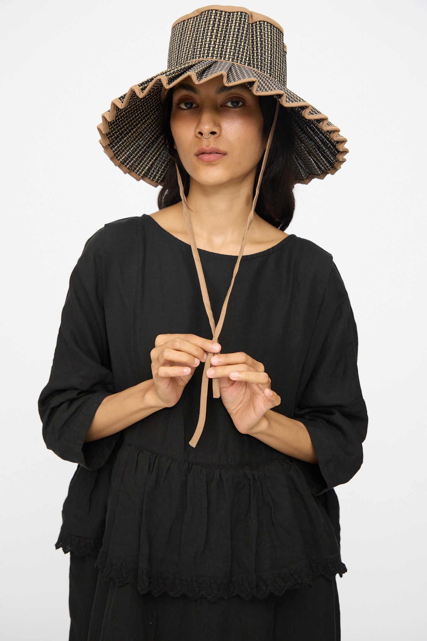 A person wearing the Lorna Murray Island Capri Maxi Hat in Nara, styled with chin ties and a loose black top, stands against a plain white background.