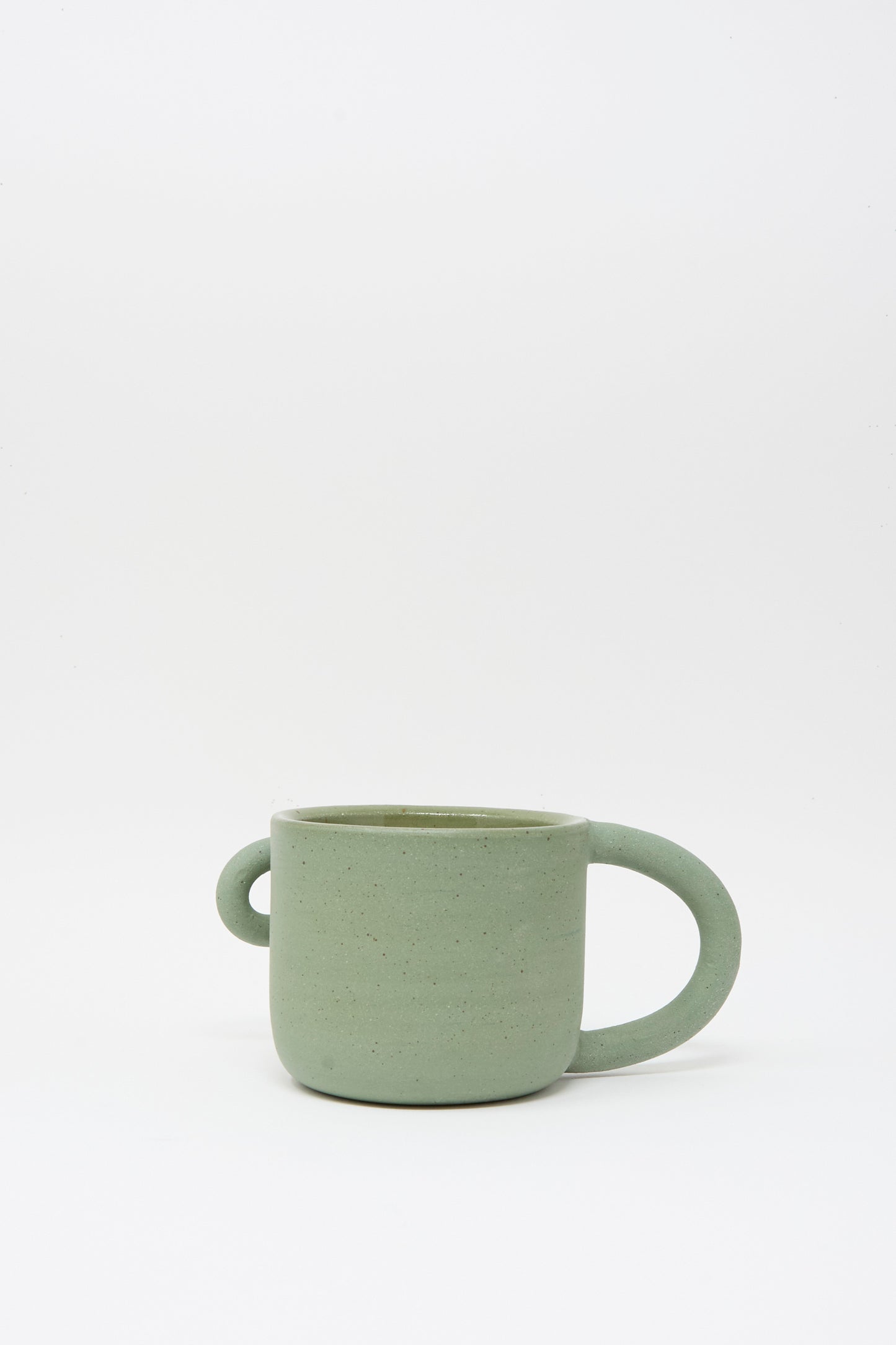 The Lost Quarry Hand Built Bow Mug in Sage is a green ceramic mug with a sage glaze, featuring two differently sized handles—one oversized—displayed on a plain white background.
