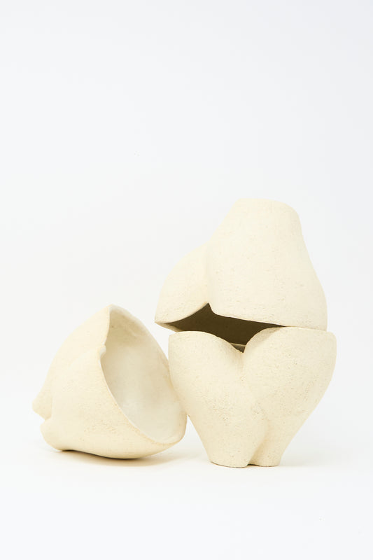 Two abstract, cream-colored Textured Clay Hand Built Bowls by Lost Quarry with organic curves sit on a white background. Each unique piece features raw, textural clay—one bowl is upright, the other tilted on its side.