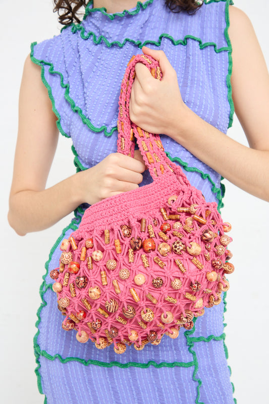 A woman is holding a Luna Del Pinal Assorted Wooden Beads Macrame Hammock Bucket Bag in Fushcia.