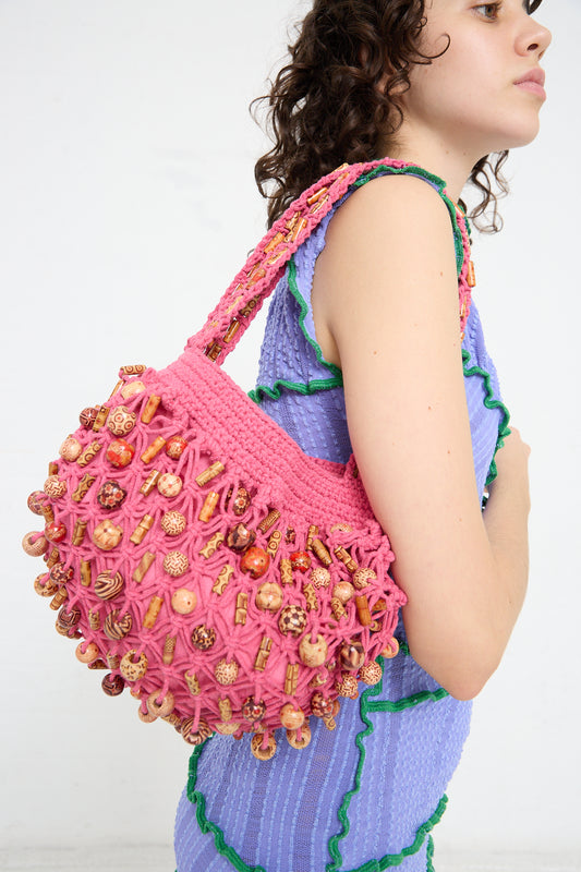A woman is holding a pink crocheted Luna Del Pinal Assorted Wooden Beads Macrame Hammock bucket bag in Fushcia.