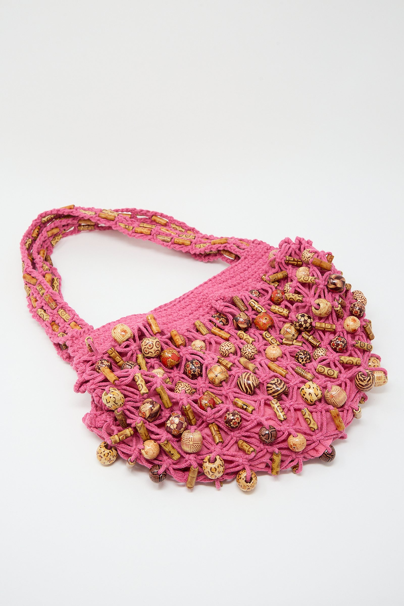 Pink knitted handbag adorned with small Luna Del Pinal assorted wooden beads on a white background.