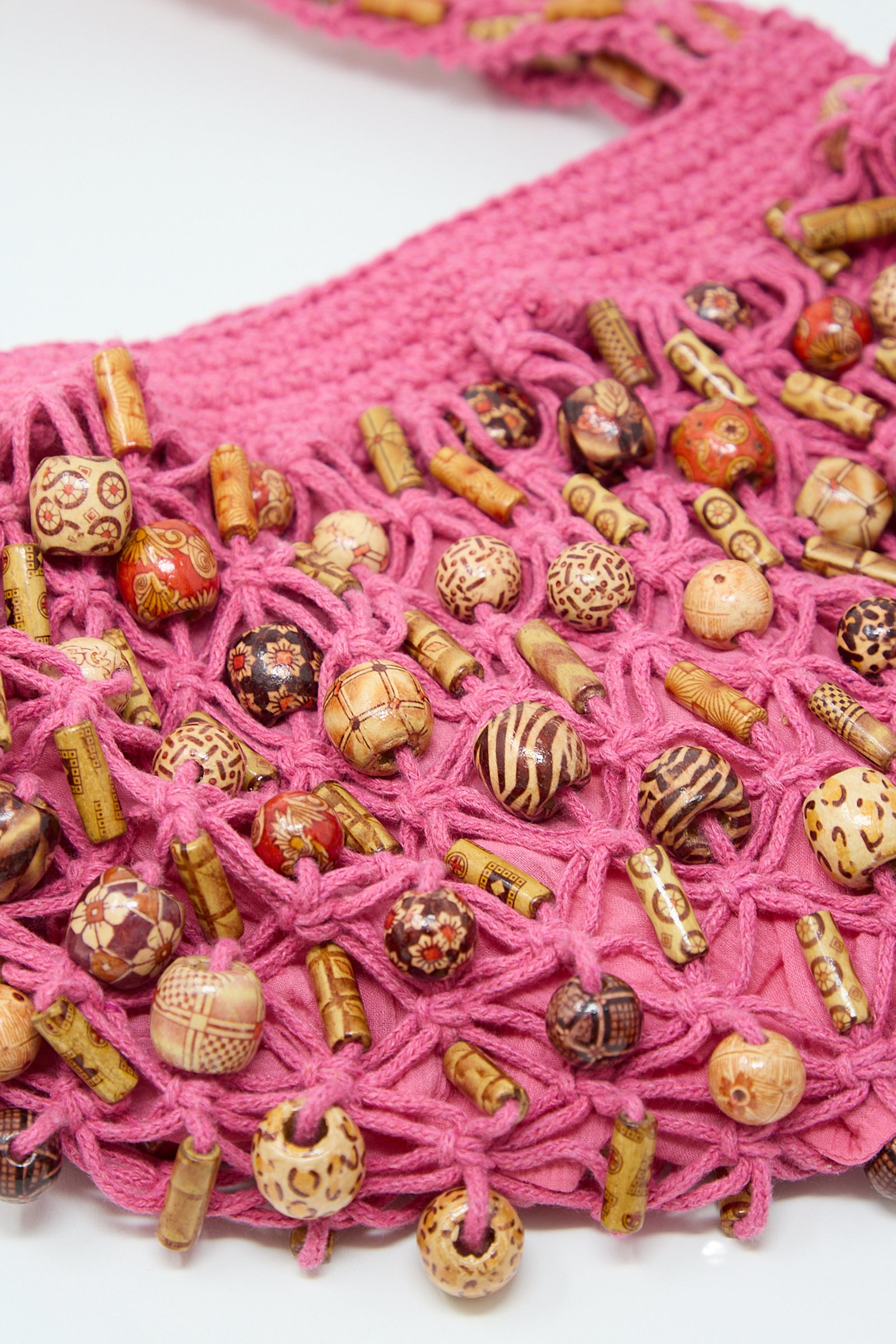 Close-up of a pink crocheted Assorted Wooden Beads Macrame Hammock Bucket Bag in Fushcia with decorative wooden beads and spools interwoven by Luna Del Pinal.
