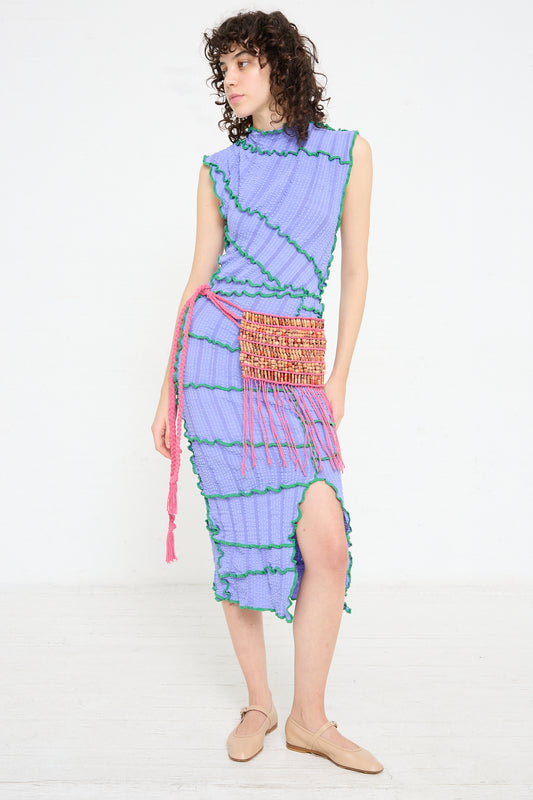 The model is wearing a purple dress with a Cotton and Assorted Bead Macrame Fringe Belt in Fuchsia by Luna Del Pinal.