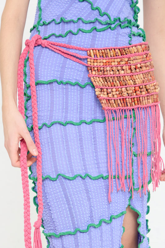 A woman wearing a purple dress with a Luna Del Pinal Cotton and Assorted Bead Macrame Fringe Belt in Fushcia.