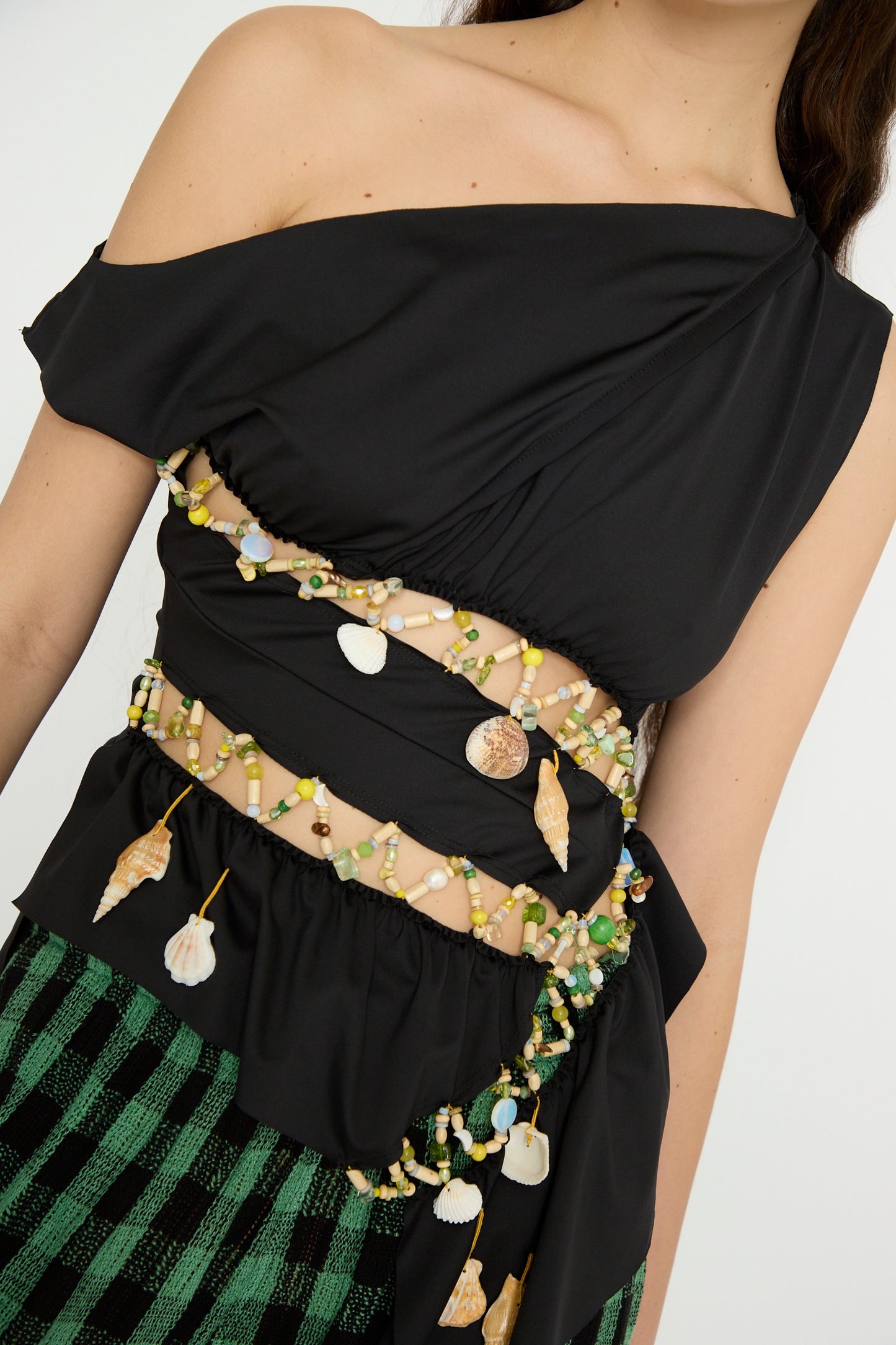 A chic ensemble featuring the Luna Del Pinal Ornamental Off Shoulder T-Shirt in Night Sea with shell and bead embellishments made from recycled polyester, paired perfectly with green and black checkered pants.
