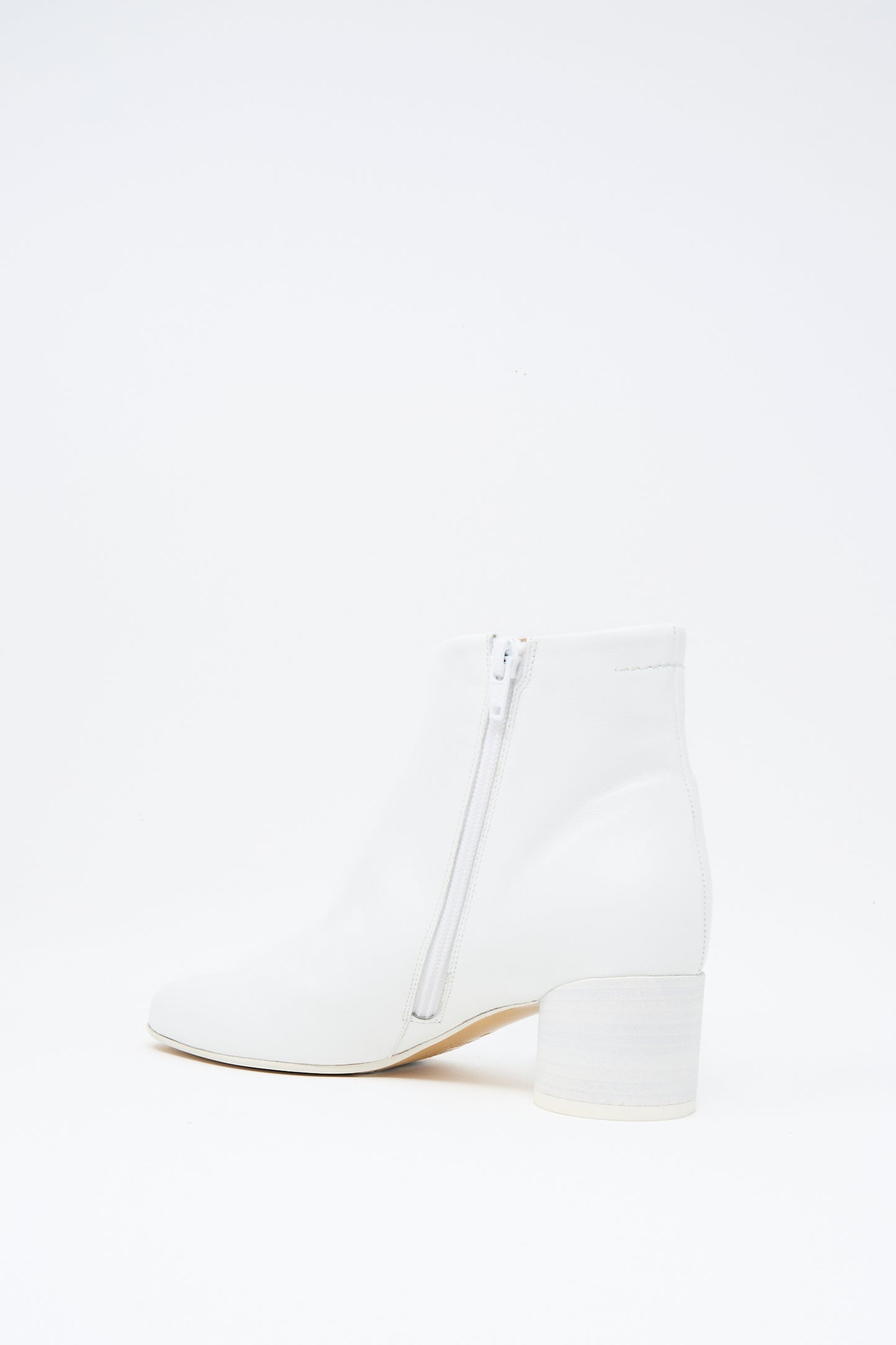 The MM6 Ankle Boot in White features a square toe, block heel, and side zipper. Crafted from buffed calfskin leather, the ankle-high boot is shown against a plain white background.