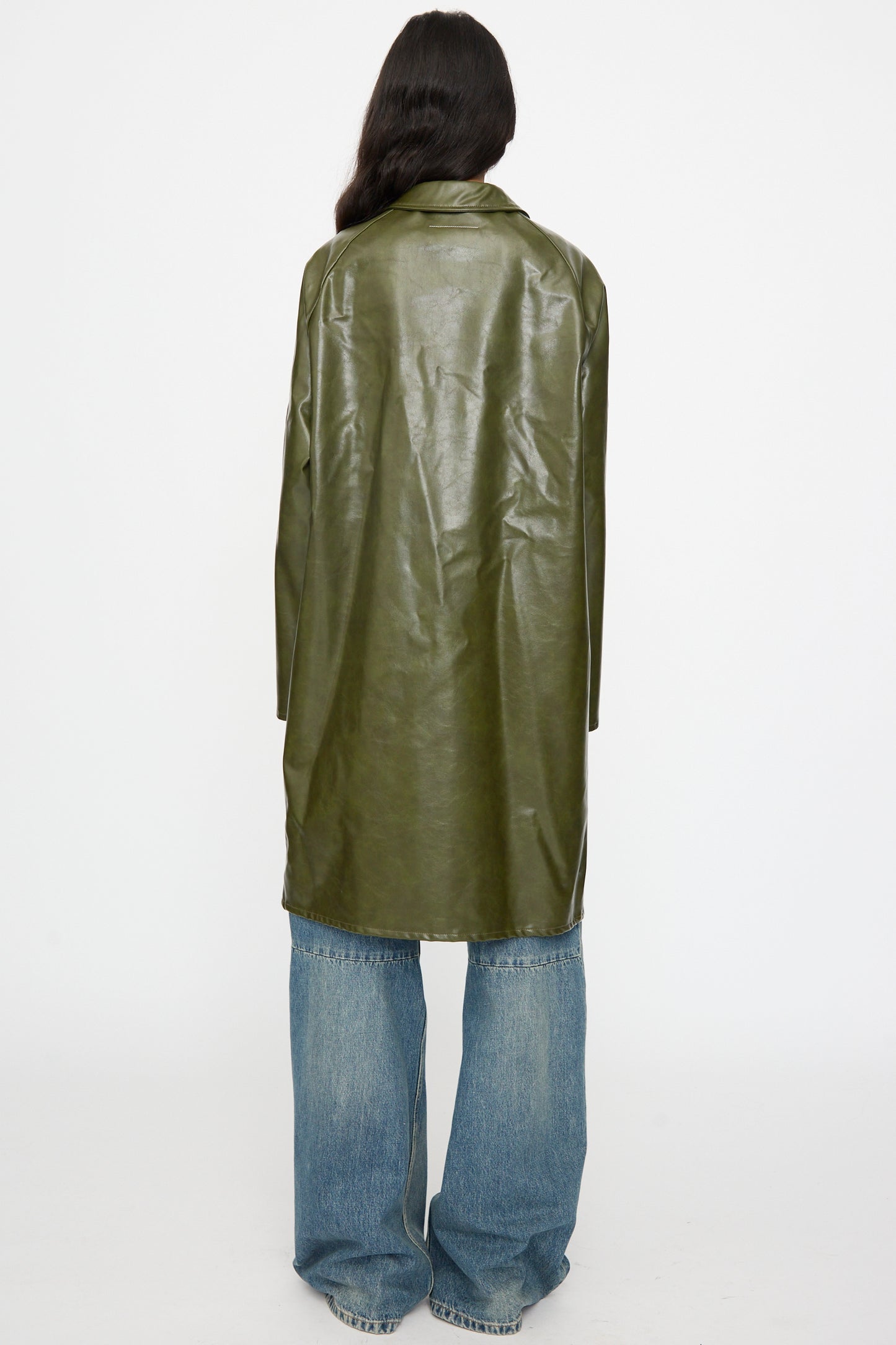 A person faces away from the camera wearing the MM6 Coat in Forest Green and wide-leg blue jeans, set against a plain white background.