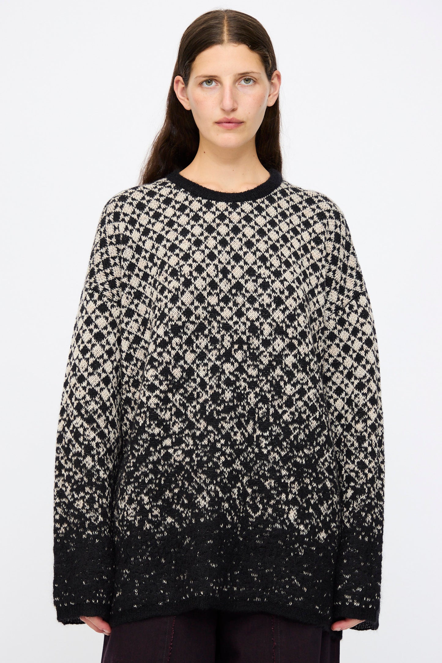 A person with long dark hair wears the MM6 Crewneck in Black and Beige, an oversized pullover with an abstract fade pattern, standing against a plain white background.