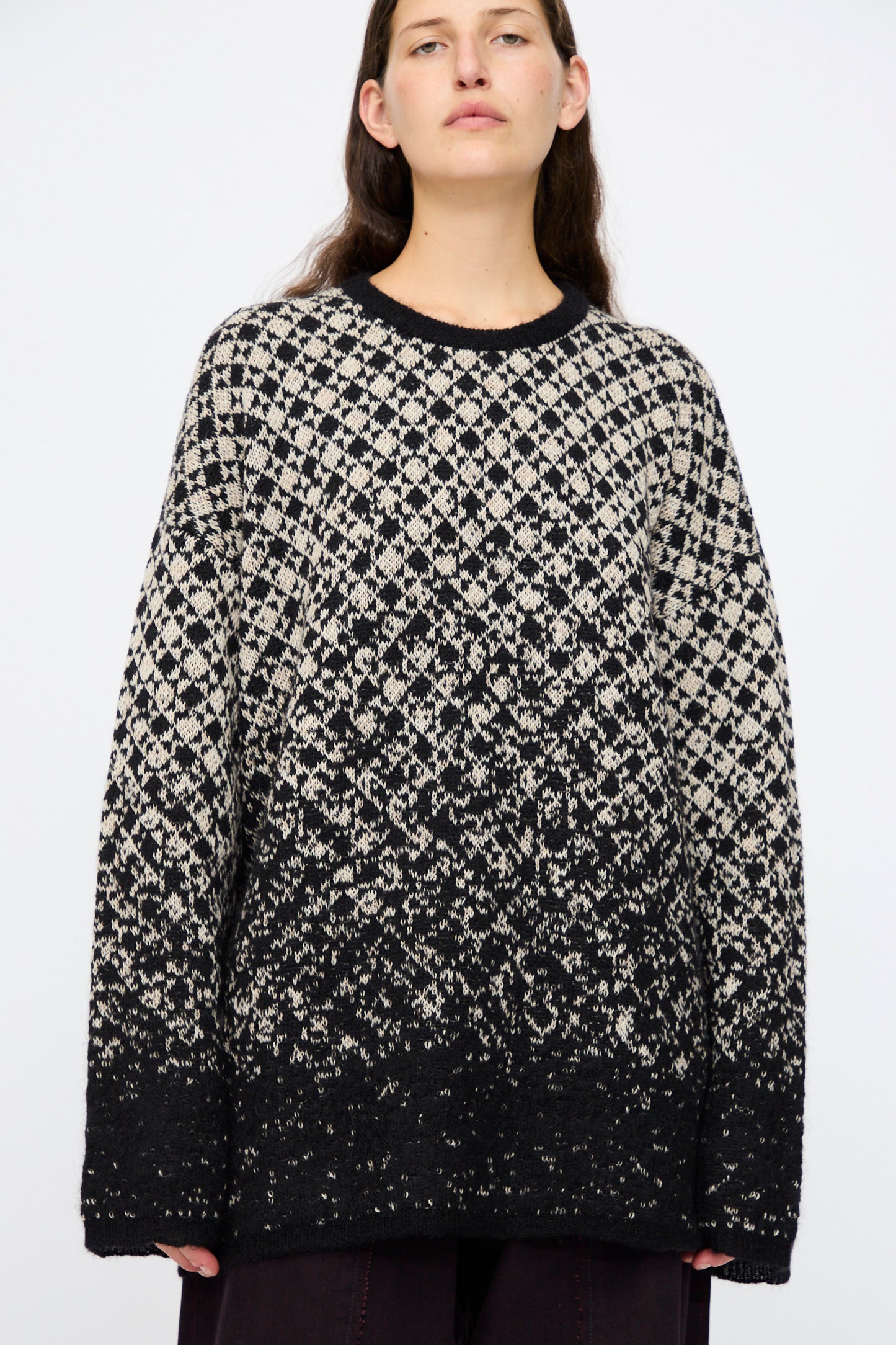 A person wears the MM6 Crewneck in Black and Beige, featuring a bold abstract pattern, standing against a plain light background.