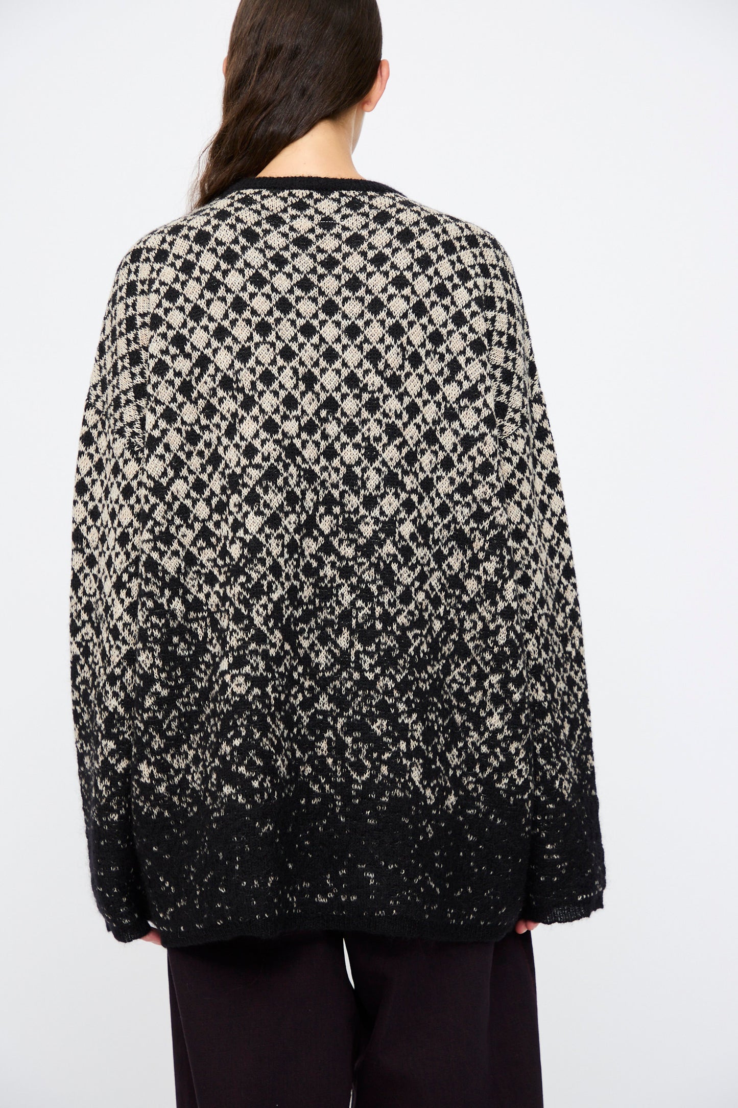 A person with long brown hair, seen from behind, wears the MM6 Crewneck in Black and Beige with an abstract pattern, paired with black pants against a plain light background.