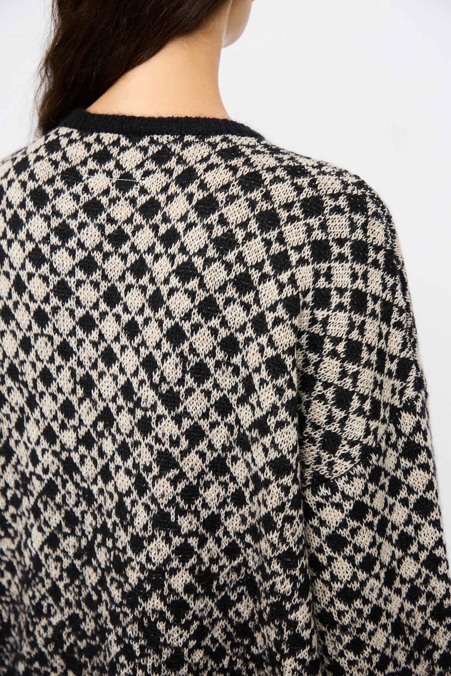 Close-up of a person wearing the MM6 Crewneck in Black and Beige, photographed from behind to showcase its textured fabric and diamond-patterned abstract design.