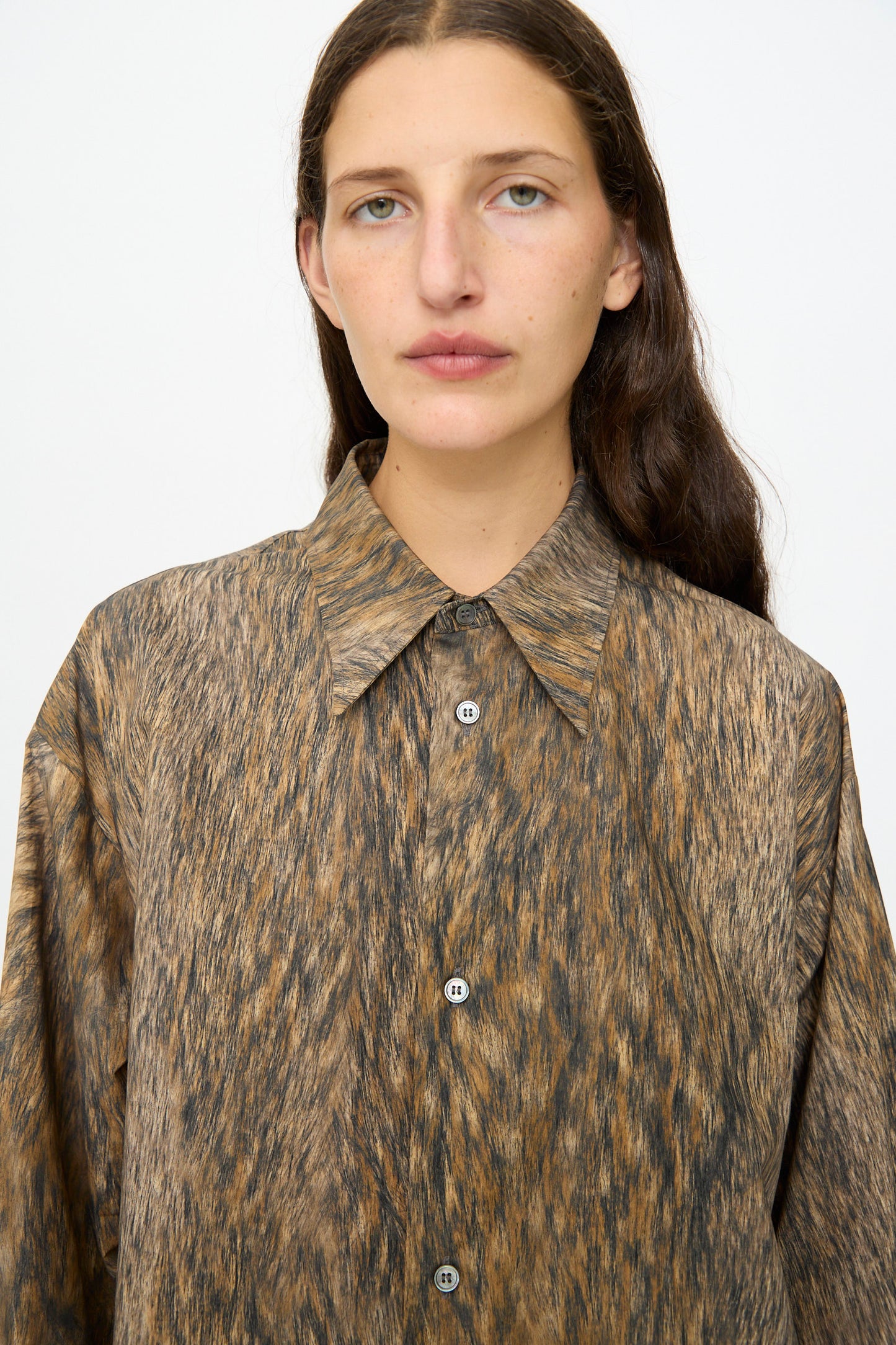 A person with long brown hair wears the MM6 Dress in Brown, featuring a loose animal print design, and looks at the camera against a plain background.
