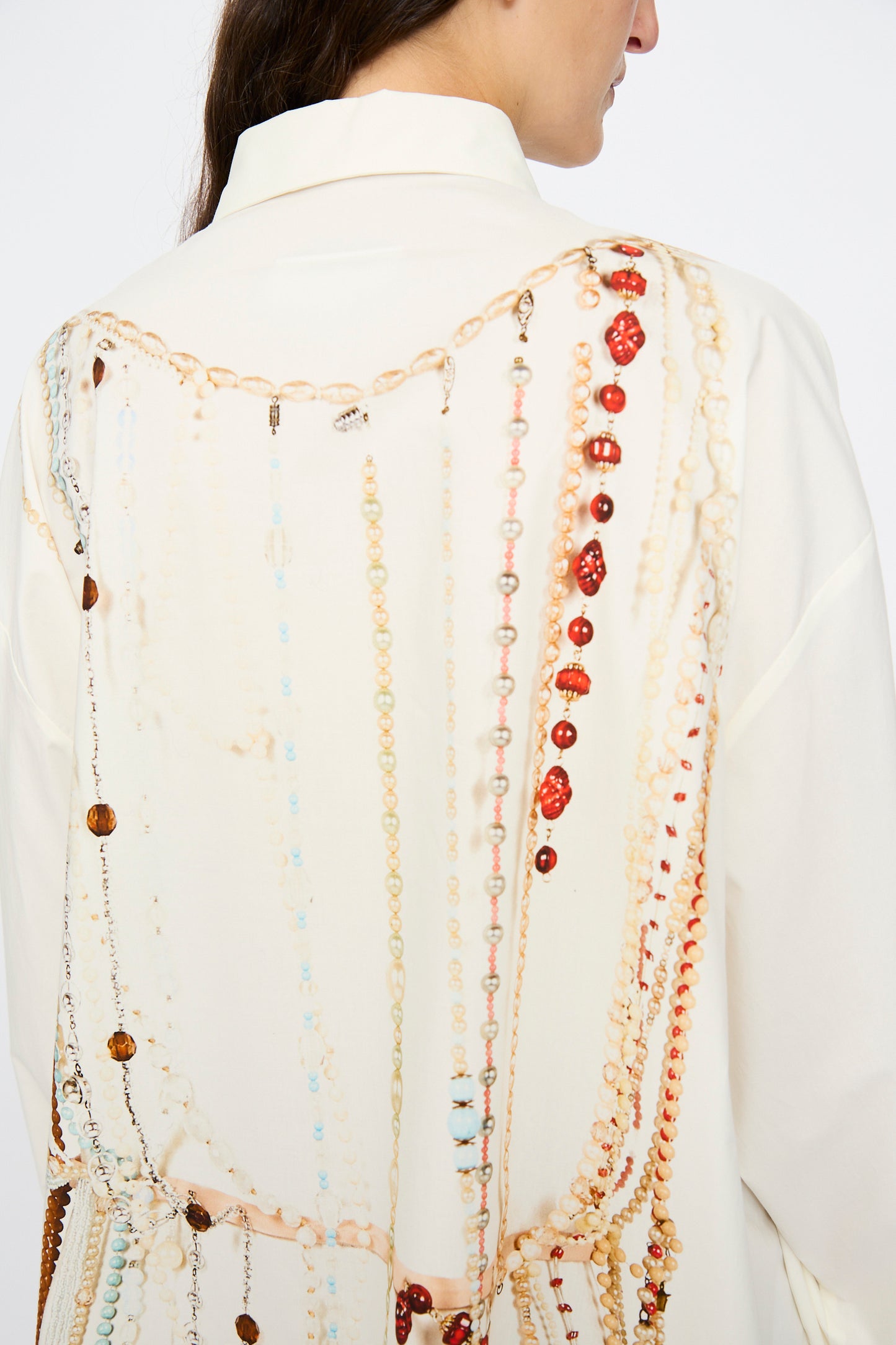 A person wearing the MM6 Dress in Pearls Print, an off-white oversized piece featuring a design of colorful beads and chains draped across the back.