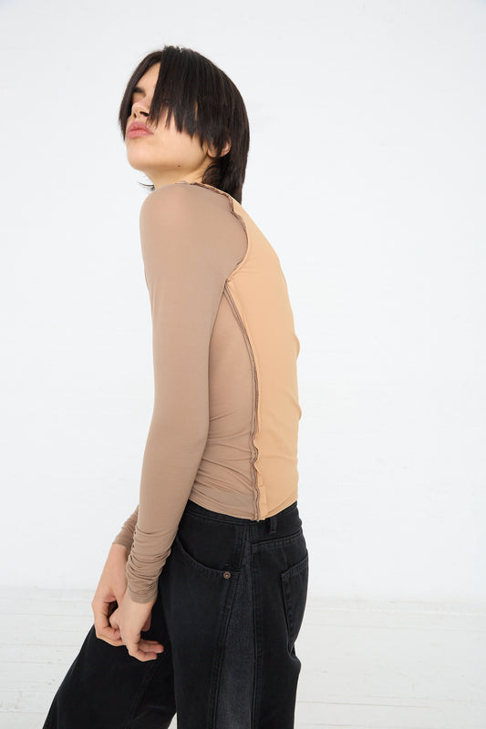 Woman posing in an MM6 long sleeve top in beige and black jeans against a white background.