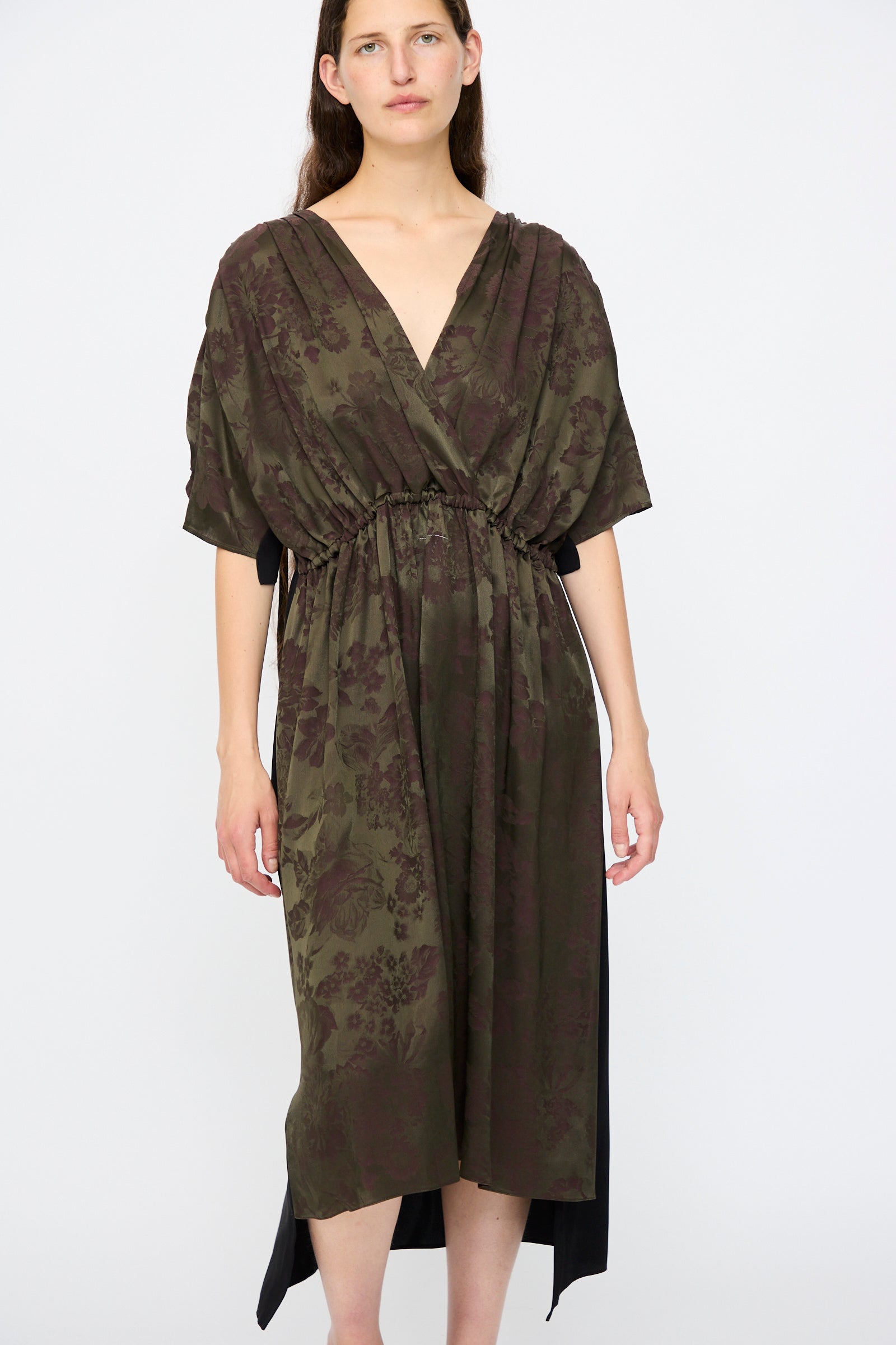 A woman wears the MM6 Midi Dress in Black and Khaki Burgundy, featuring a relaxed fit, floral print, gathered waist, and short sleeves, standing against a plain white background.