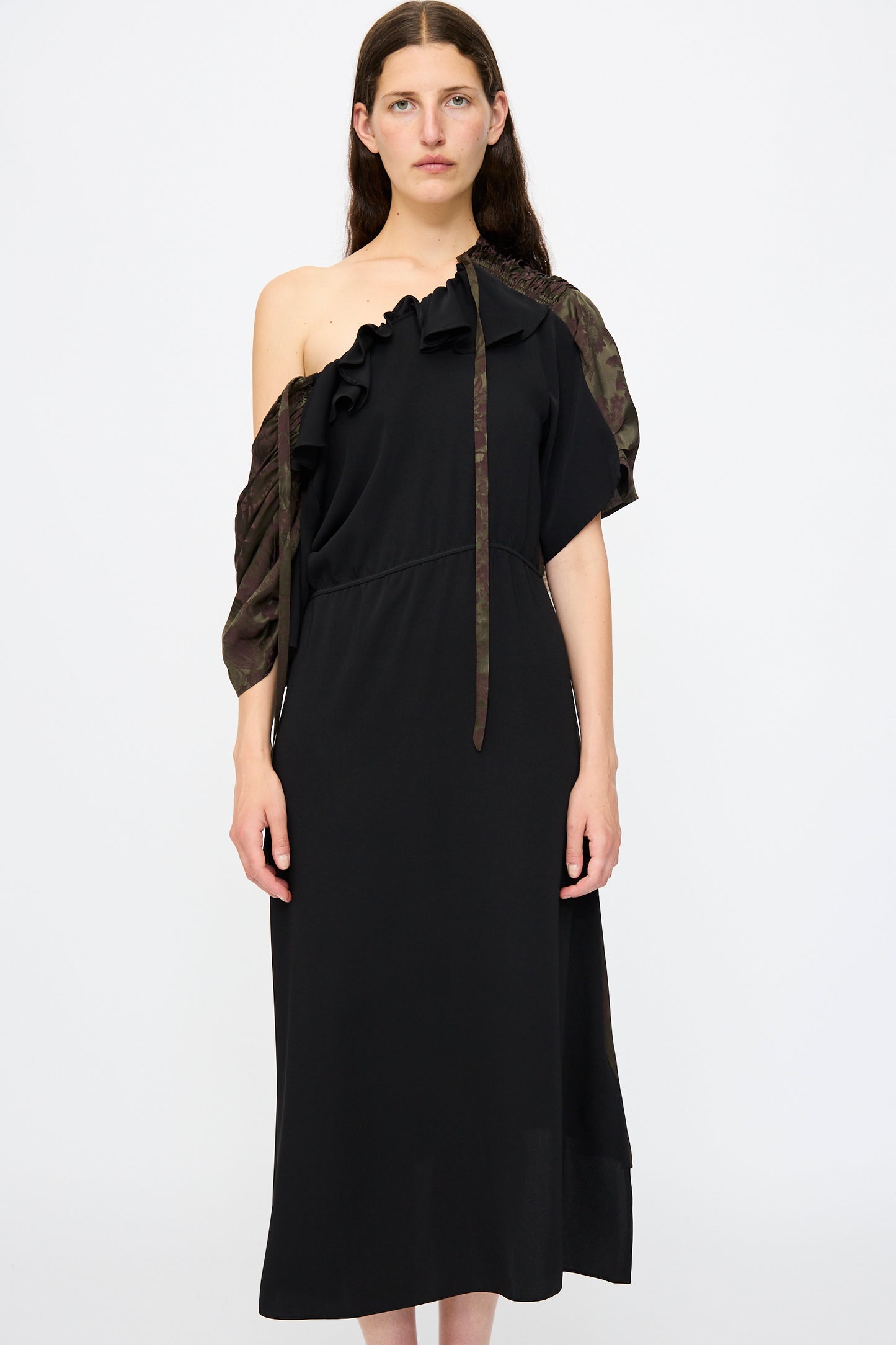 A woman wears the MM6 Midi Dress in Black and Khaki Burgundy, featuring a one-shoulder design with ruffled detailing, an asymmetric sleeve, drawstring shoulder, and a relaxed fit for effortless elegance.