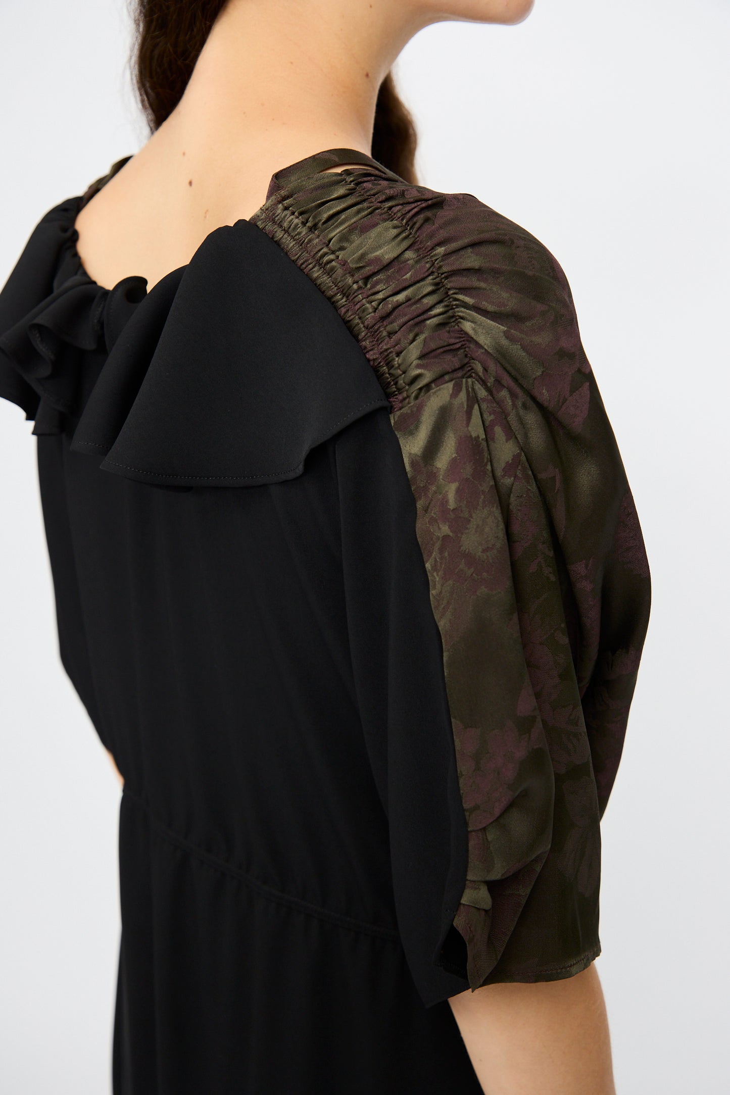 A close-up of a person wearing the MM6 Midi Dress in Black and Khaki Burgundy, featuring floral-printed ruched sleeves, a ruffled neckline, and a relaxed fit.