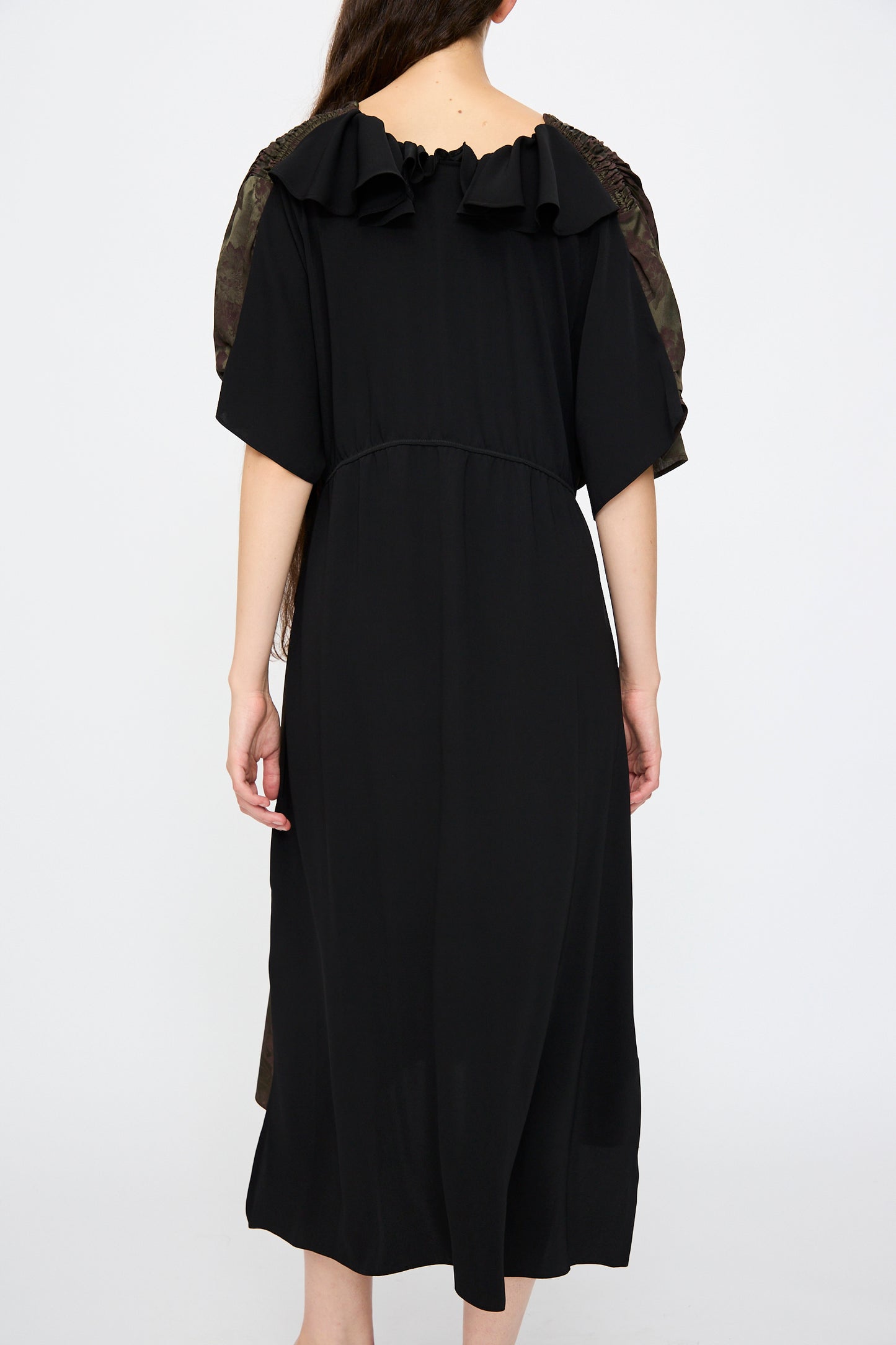 A woman wearing the MM6 Midi Dress in Black and Khaki Burgundy stands facing away, showing off its short sleeves and ruffle details.