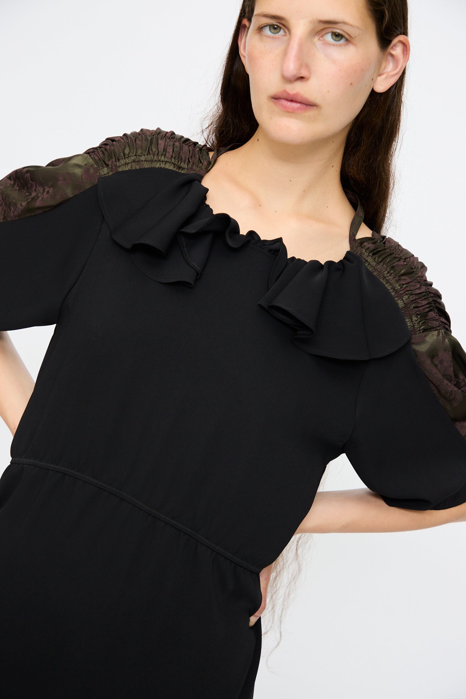 A woman models the MM6 Midi Dress in Black and Khaki Burgundy, featuring a relaxed fit with ruffled neckline and gathered shoulder detailing, set against a plain light background.