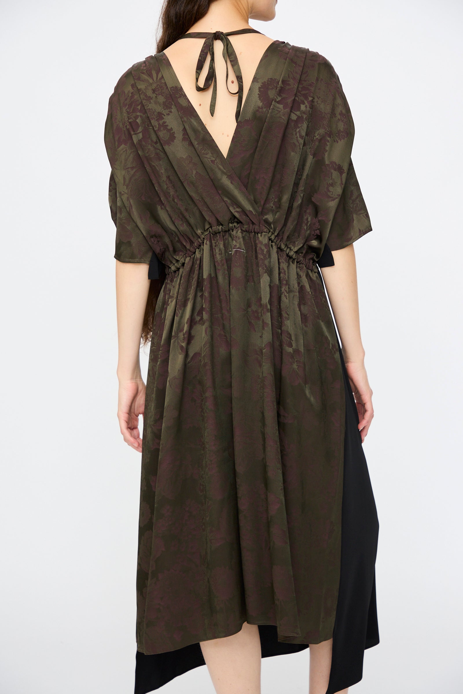 A person is seen from behind in the MM6 Midi Dress in Black and Khaki Burgundy, featuring a relaxed fit, cinched waist, floral print, and a back neck tie.