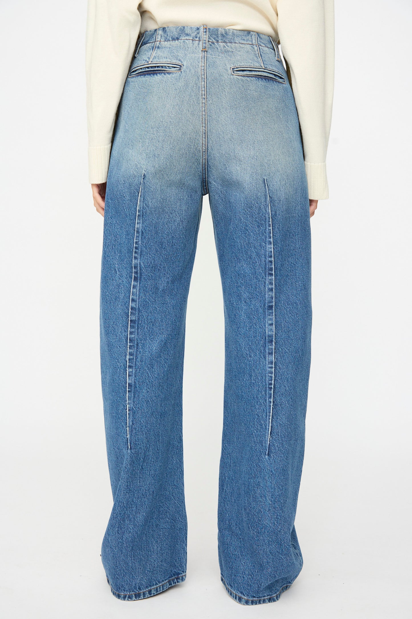 Model is seen from the back wearing MM6’s Pants in Blue, featuring a relaxed fit, high-waisted wide-leg silhouette with vertical seams and two welt pockets at the rear, crafted from subtly faded denim.