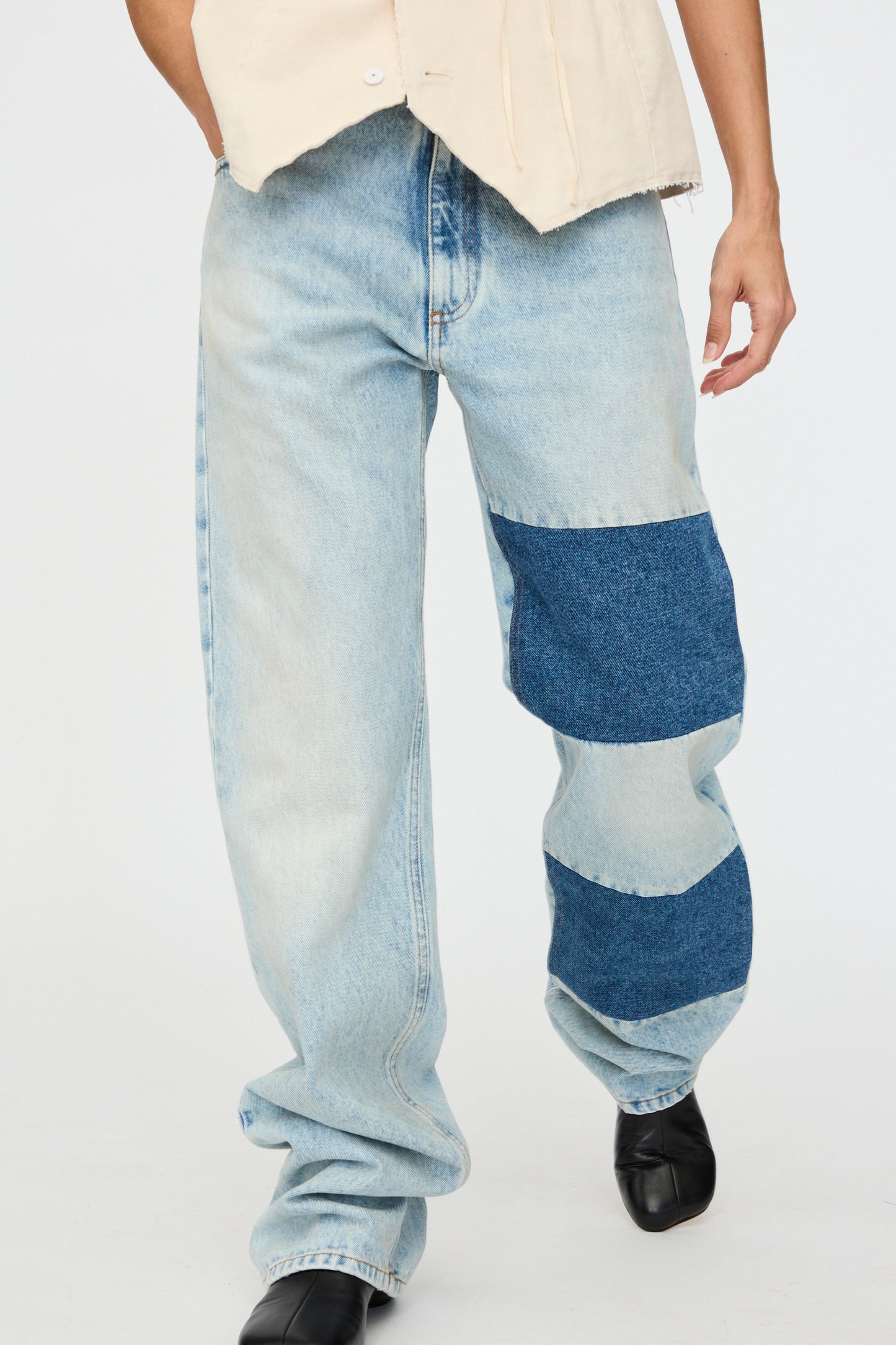 Someone is wearing MM6 Pants 5 Pockets jeans showcasing patchwork denim with two large dark blue patches on one leg, teamed up with a sleeveless beige top and black shoes.