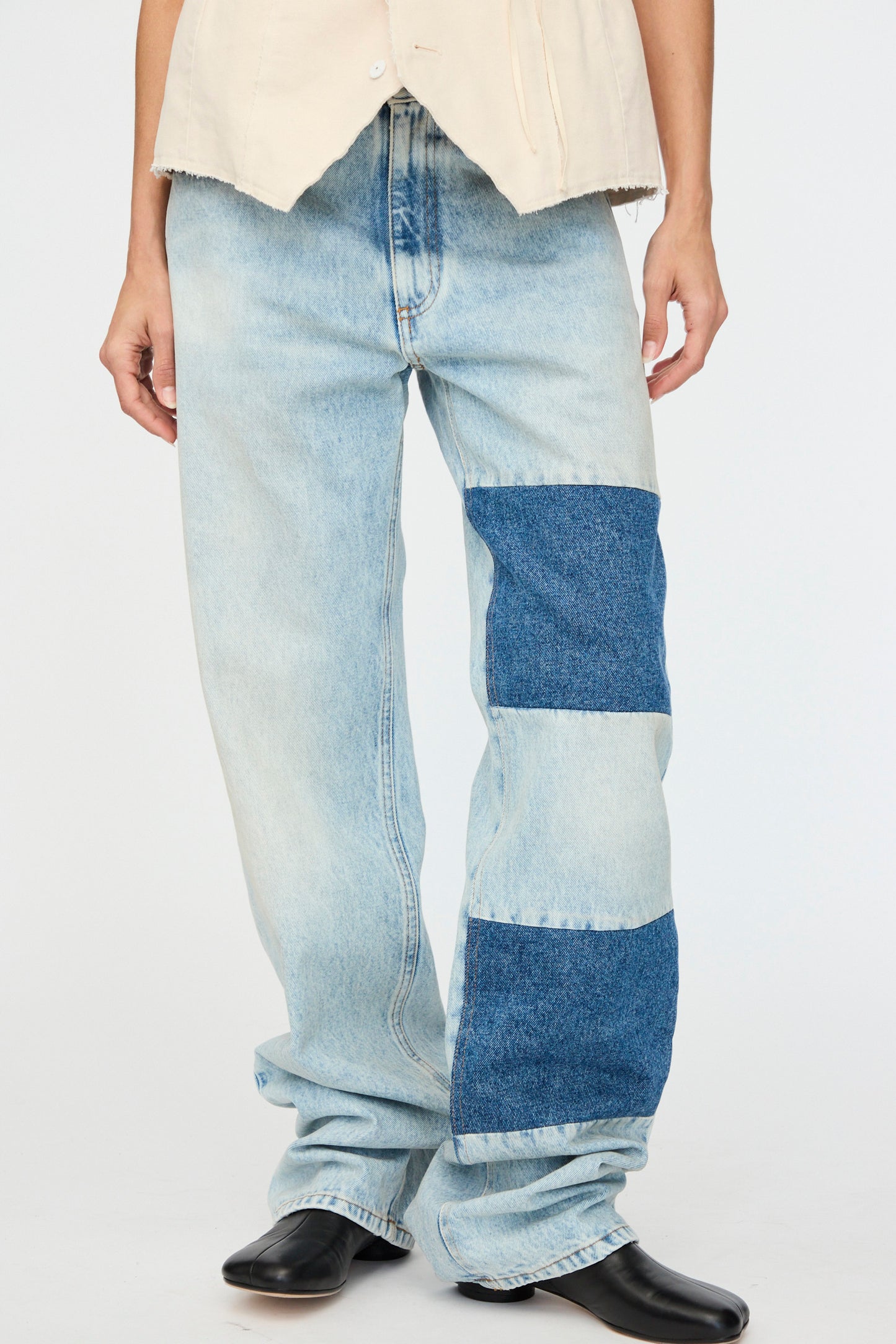 An individual in MM6's Pants 5 Pockets, featuring a relaxed fit with light blue, patchwork denim details, pairs them with black shoes against a plain backdrop.