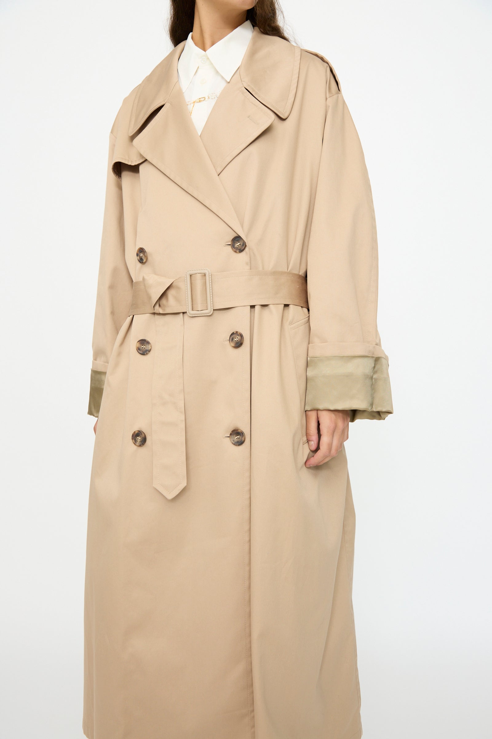 A person wearing the MM6 Trench Coat in Sand, a double-breasted cotton style with a belt and wide lapels, over a white collared shirt.