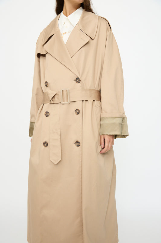 A person wearing the MM6 Trench Coat in Sand, a double-breasted cotton style with a belt and wide lapels, over a white collared shirt.