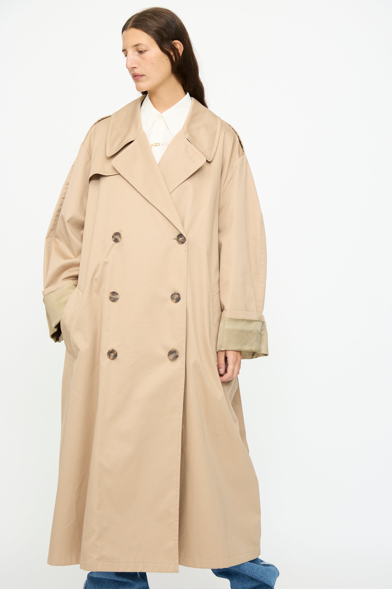 A person in the MM6 Trench Coat in Sand, worn over a white shirt and blue jeans, stands against a plain white background.