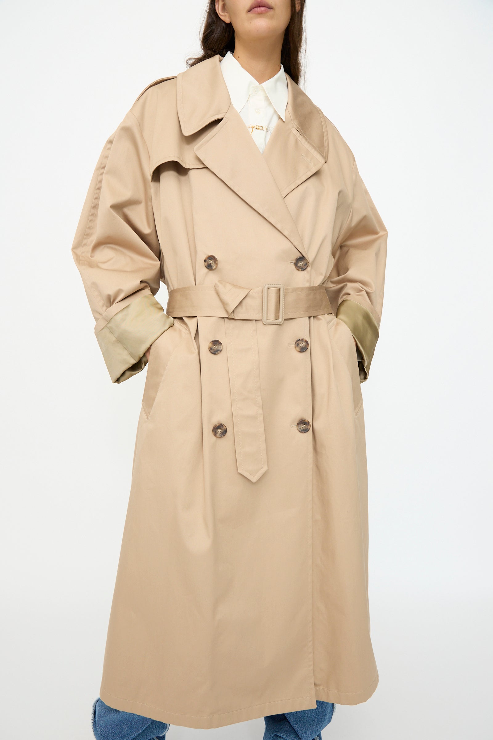 Model wears the MM6 Trench Coat in Sand, double-breasted and belted, over a white shirt and blue jeans, against a plain white background.