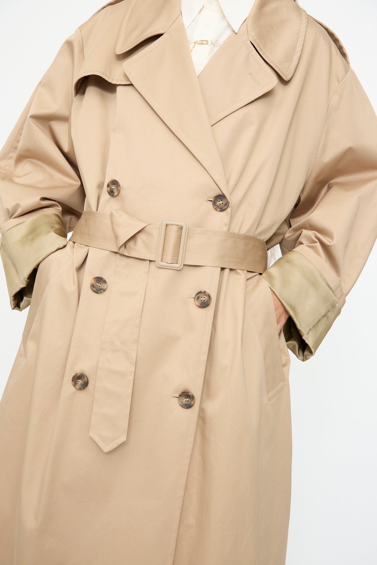 Model wearing the MM6 Trench Coat in Sand, an Italian-made, double-breasted style with belt, shown from neck to mid-thigh against a plain background and hands in pockets.