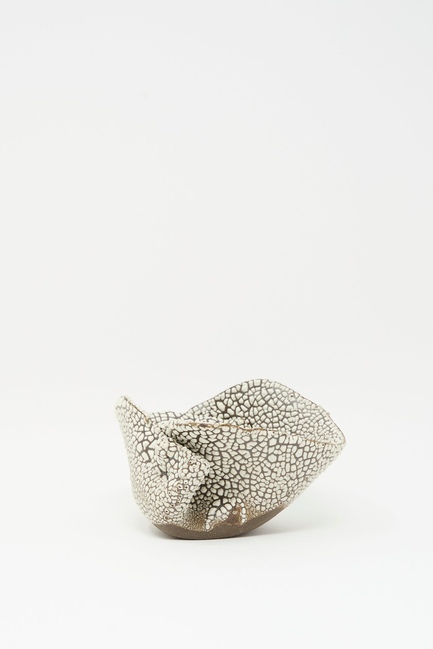 The Folded Bowl in Crawl I by MONDAYS, a hand-built piece with a cracked white glaze, sits on a plain white background, highlighting the artisanal spirit of Brooklyn craftsmanship.