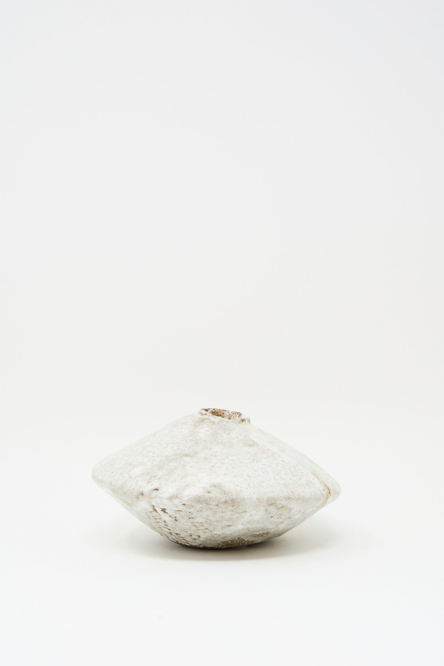 The MONDAYS Ikebana Vase in White over Dark Brown features a round, flat shape with a rough texture and subtle white glaze, evoking minimalist elegance against a plain white background.