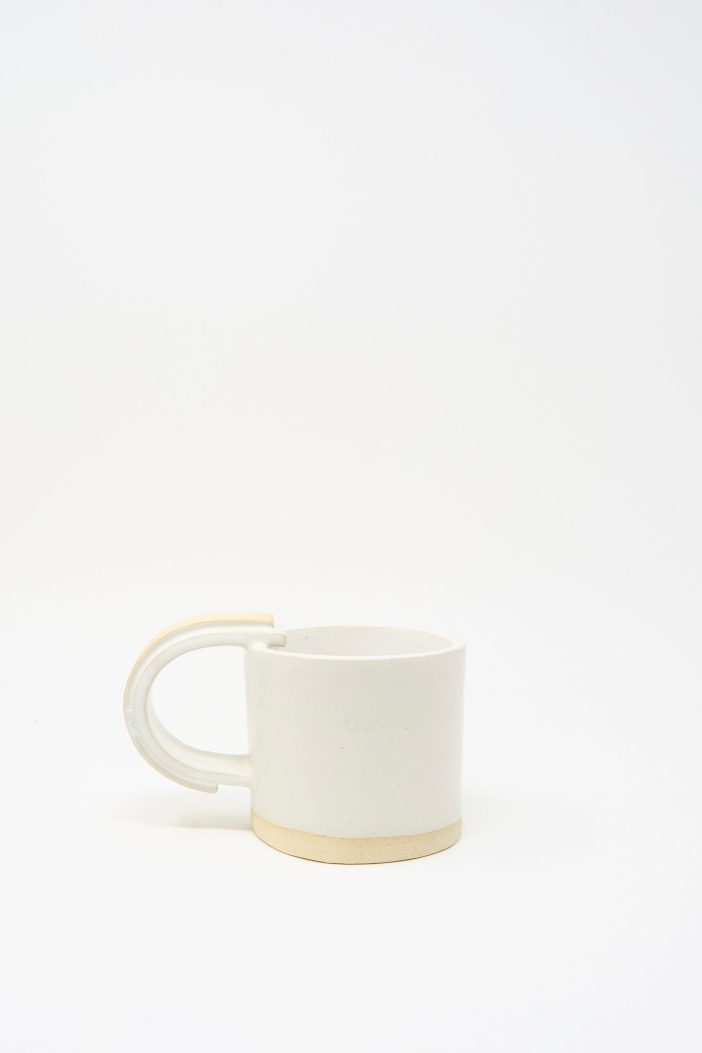 The MONDAYS Layered Mug in White on Sand features a handmade white ceramic body, beige base, and a large rounded unglazed handle, shown on a plain white background.