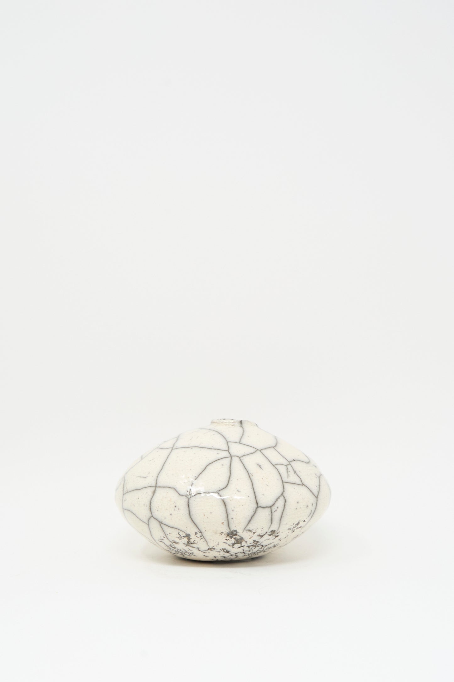 The Raku Moon Vase in White by MONDAYS is a round, white stoneware vase with a narrow opening and bold black crackle pattern, shown on a plain white background.