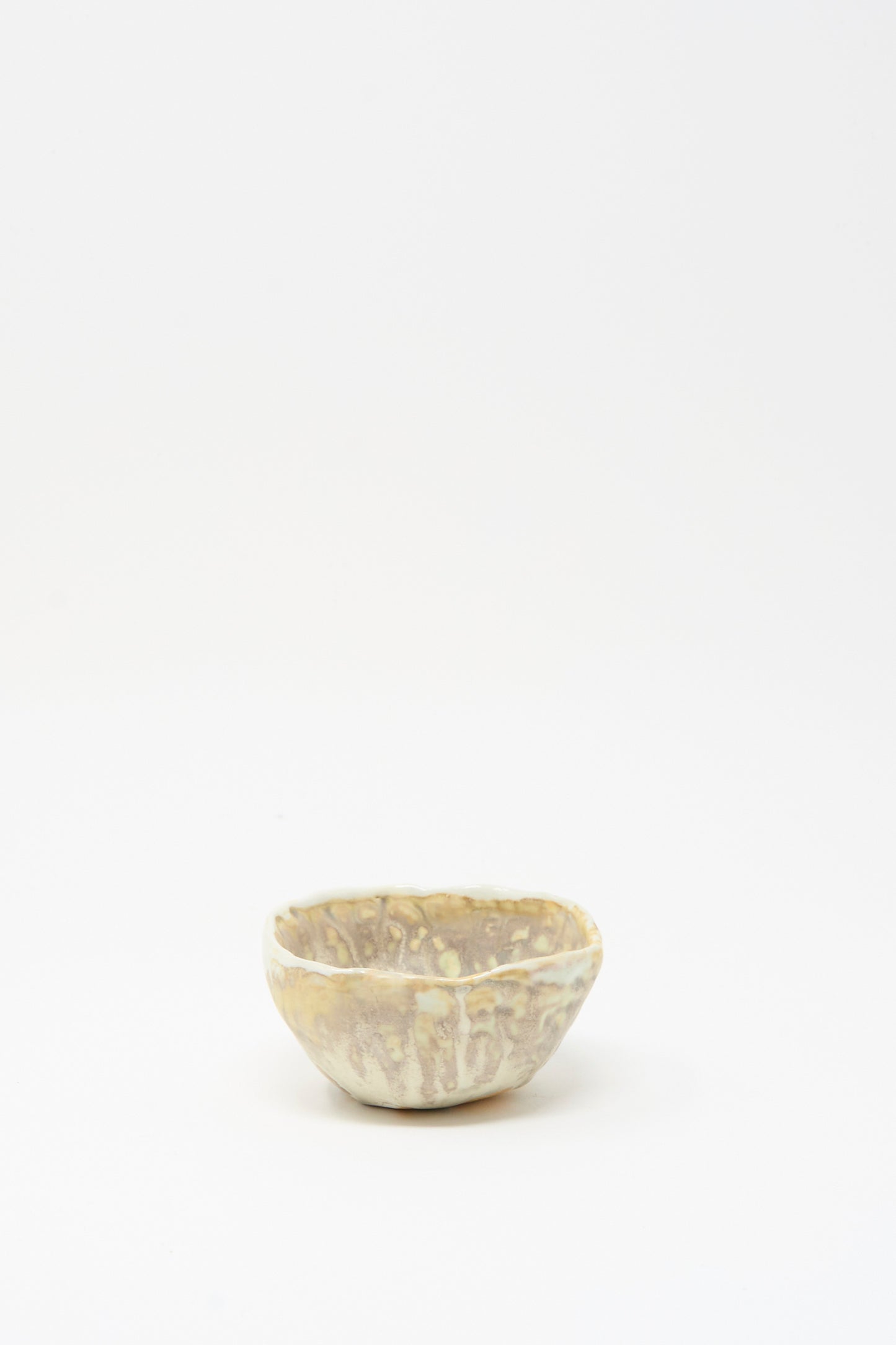 The Soda-Fired Pinched Bowl I by MONDAYS is a small, round handmade bowl featuring a textured light beige and brown surface, shown on a plain white background.