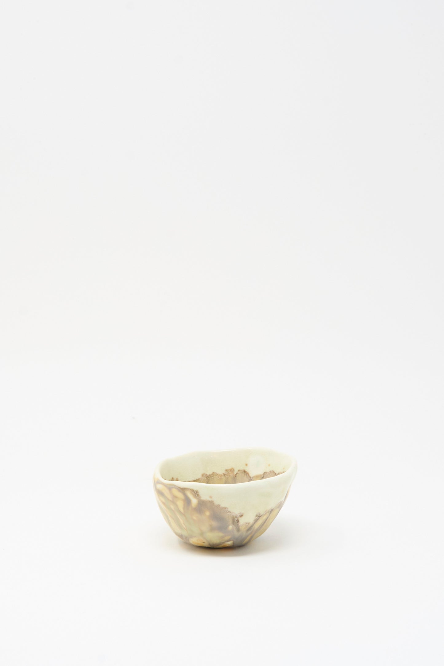 The MONDAYS Soda-Fired Pinched Bowl II is a small, handmade bowl with an uneven rim and mottled beige glaze, shown on a plain white background.