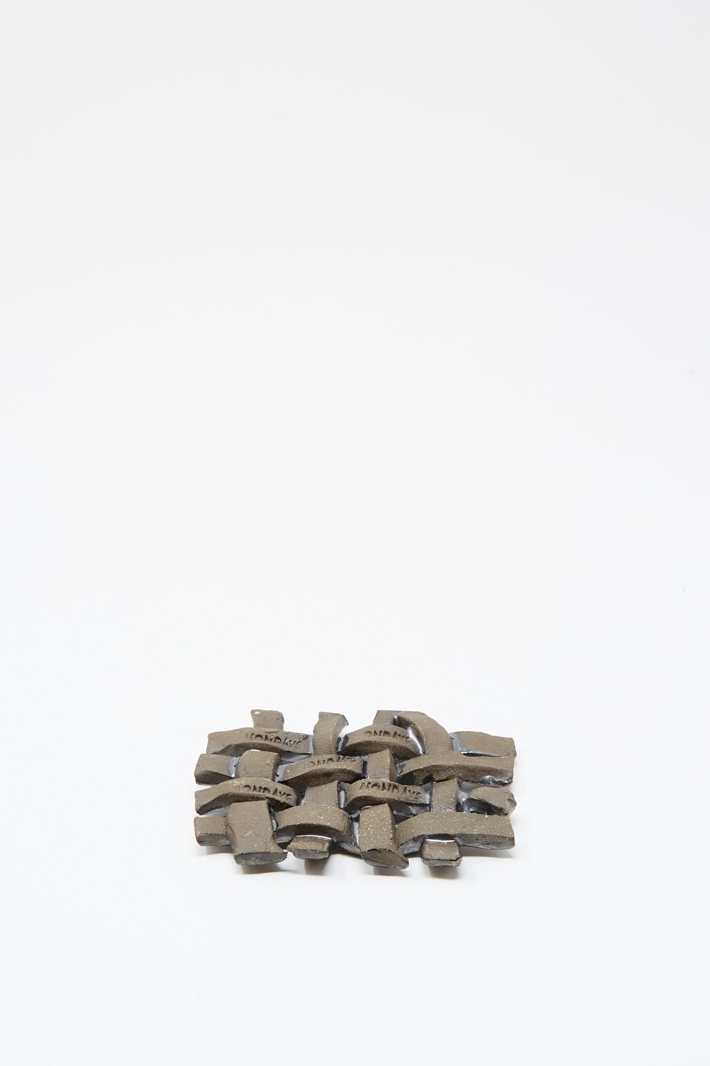 The MONDAYS Woven Dish in Charcoal is a small, rectangular ceramic piece with interwoven curves and a subtle charcoal glaze, displayed on a plain white background.