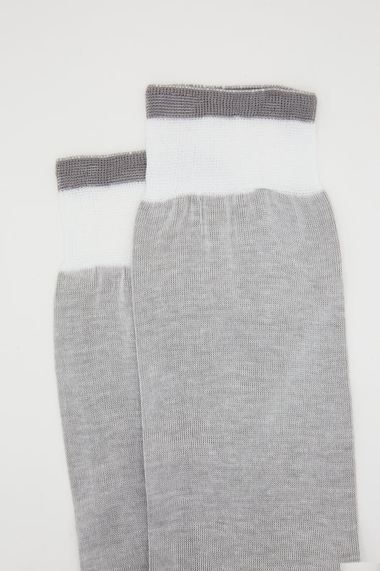 A pair of Cotton Long Sock in Grey with white tips and dark gray elastic bands, handcrafted by Maria La Rosa, laid out flat on a white background.