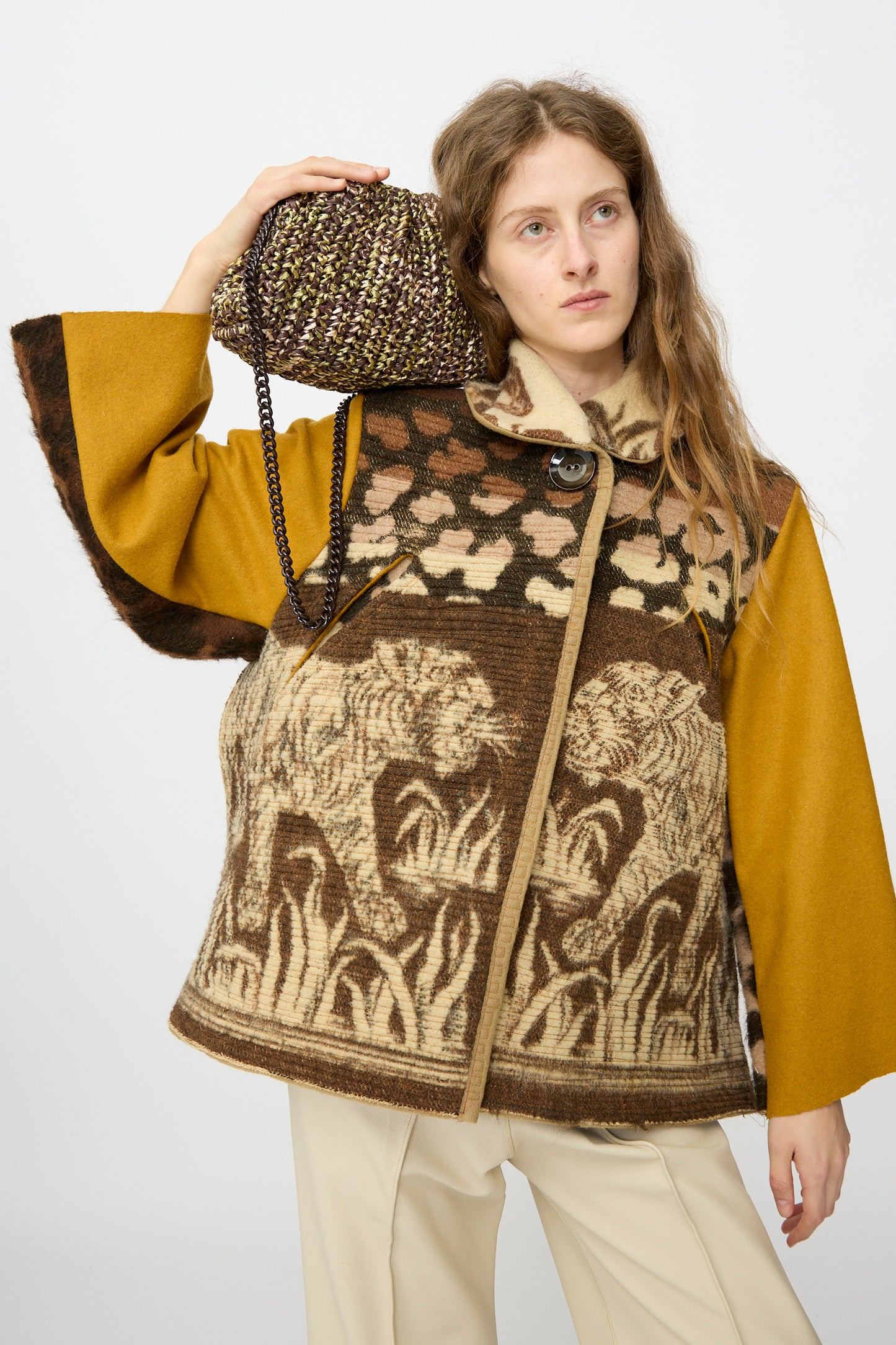 A woman wearing a brown and yellow tiger print jacket holds the Maria La Rosa Earth Game Crochet Bag in Natural on her shoulder.