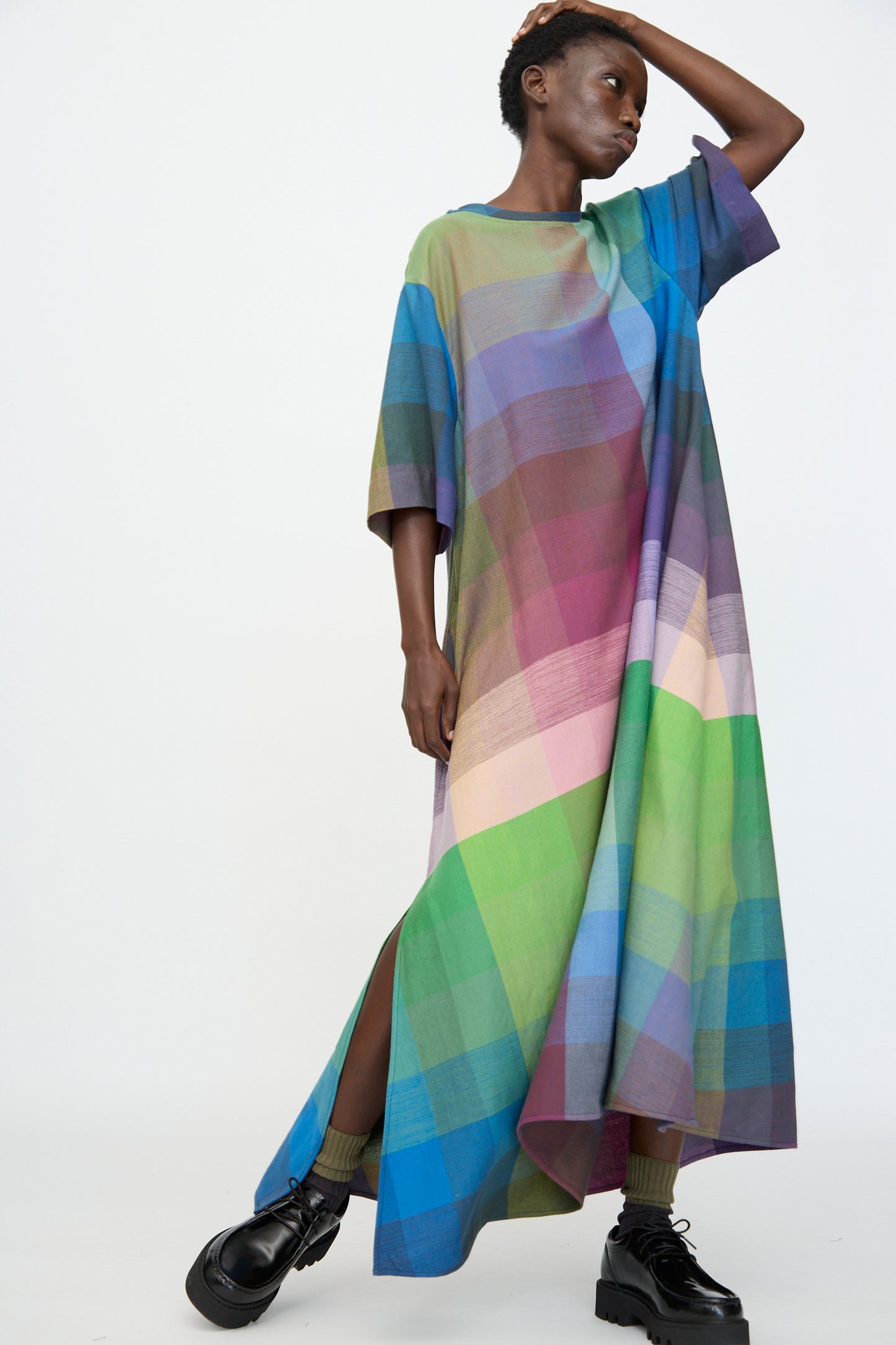 A person wears the Marrakshi Life T Shirt Dress in Plaid Multi, featuring a loose fit and short sleeves, paired with black platform shoes and standing against a plain white background.