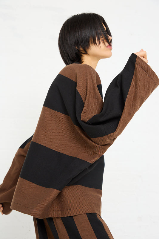 Woman in a Marrakshi Life Twill Sweater in Black and Brown Stripe posing with her arm raised.
