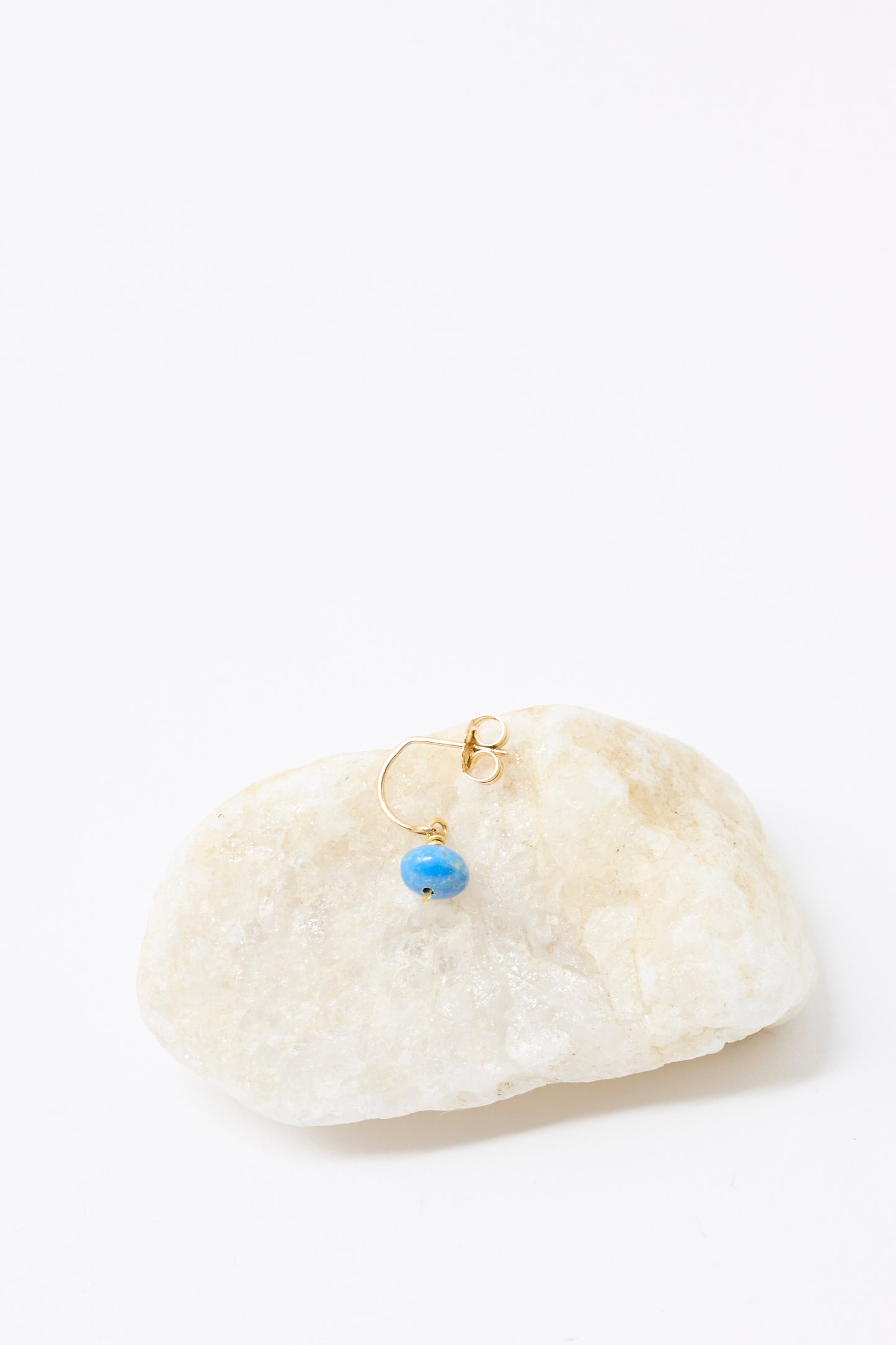 The Mary MacGill 14K Crescent Charm Single Earring in Ceruleite features a small blue bead and is shown on light-colored stone against a white background.